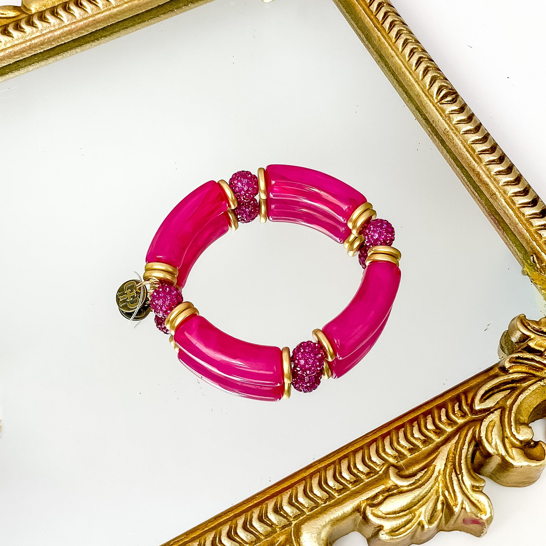 Fuchsia marbled tube bangle with gold beaded spacers. This bracelet also includes round, fuchsia crystal beads. This bracelet is pictured on a gold mirror and on a white background.