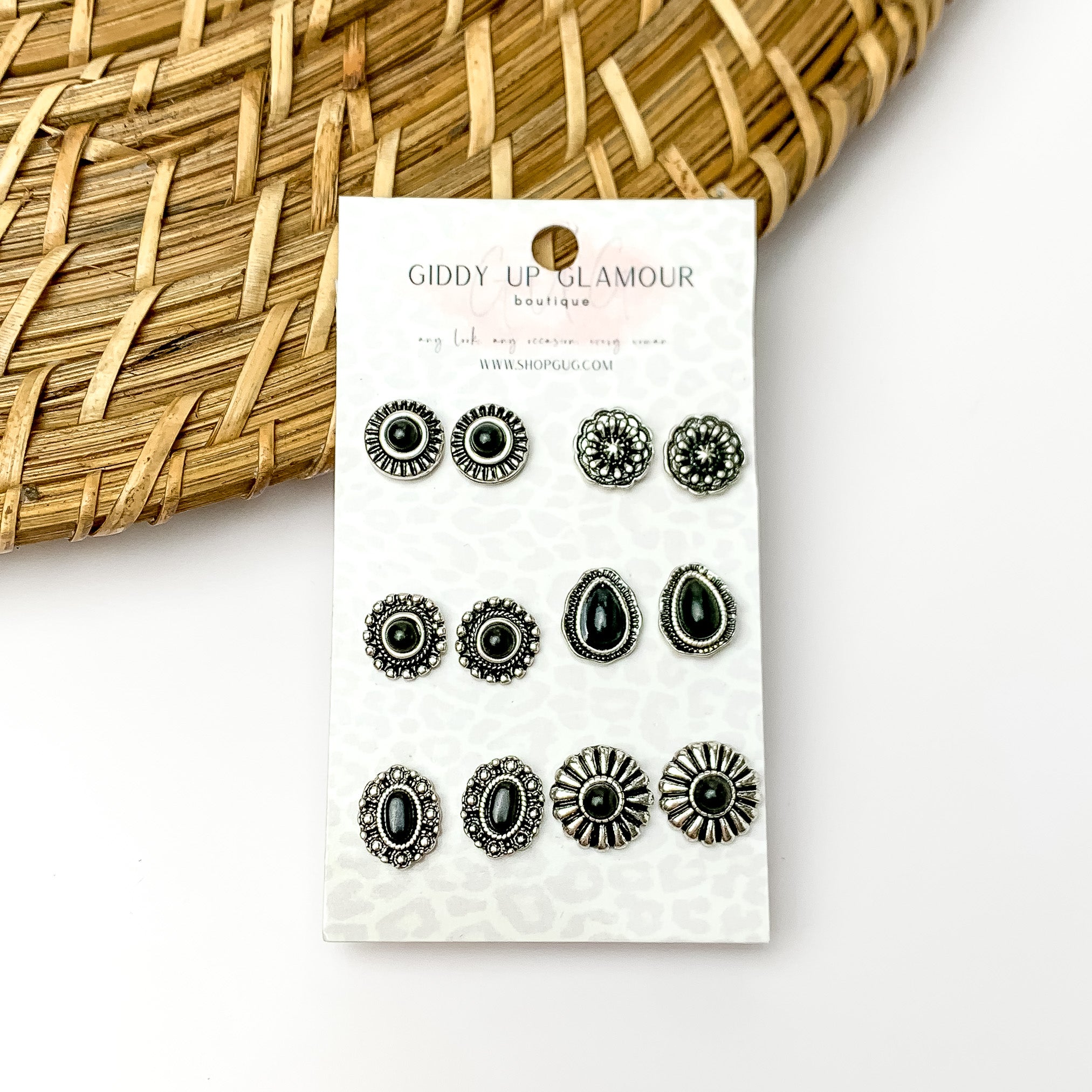 Set of six black and silver designed circular earrings. Pictured on a white background with wood like decorations in the top left corner.