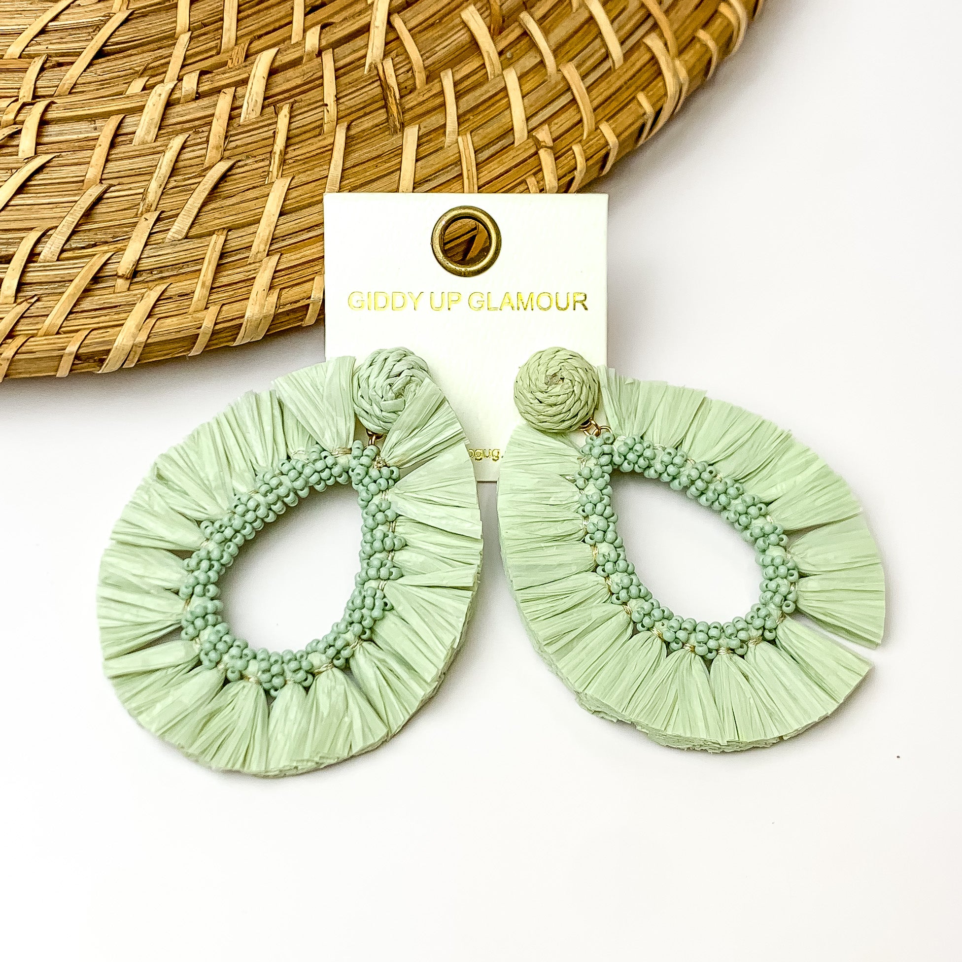 Mint green fringe open drop hoop earrings. Pictured with a white background and wood like decoration in the top left corner.
