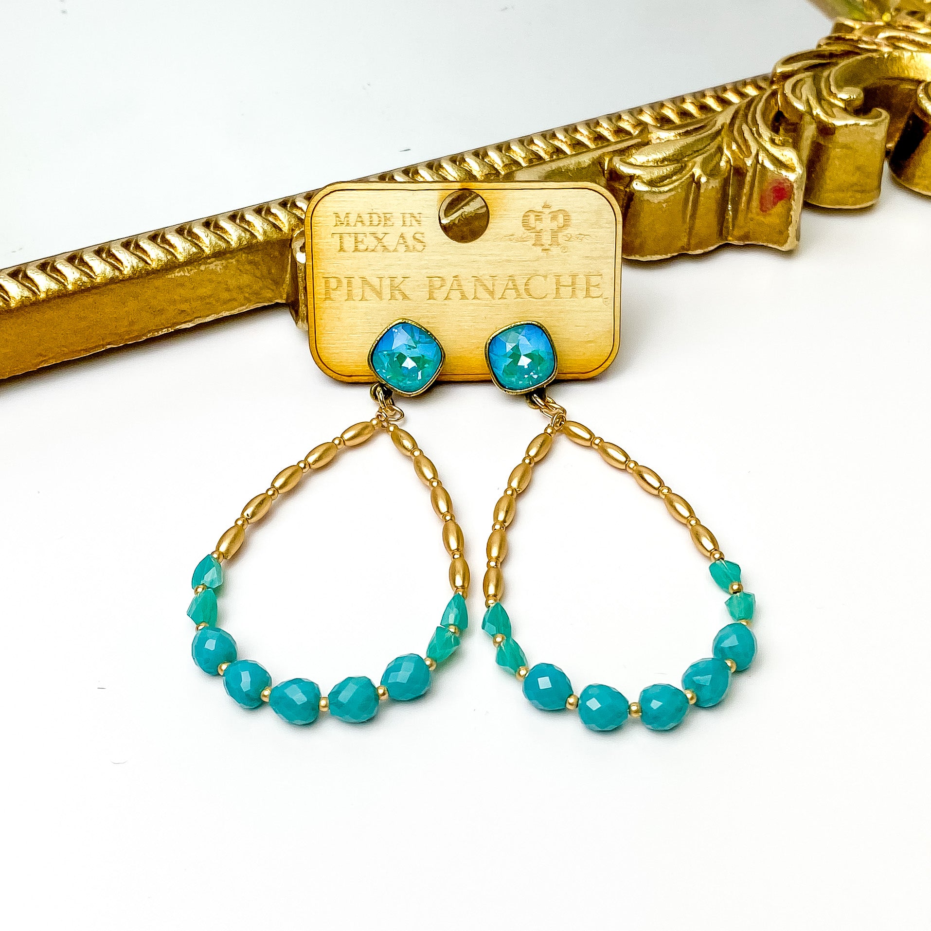 AB cushion cut post back earrings with a teardrop pendant. This pendant includes half gold beads and the bottom half has turquoise crystal beads with small gold spacers. These earrings are pictured on a wood earrings holder in front of a gold mirror on a white background. 