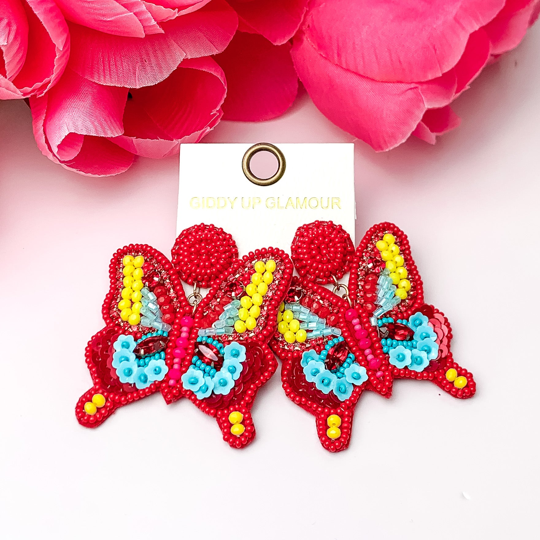 Butterfy beaded earrings in red, yellow, and blue. Pictured on a white background with pink flowers at the top. 