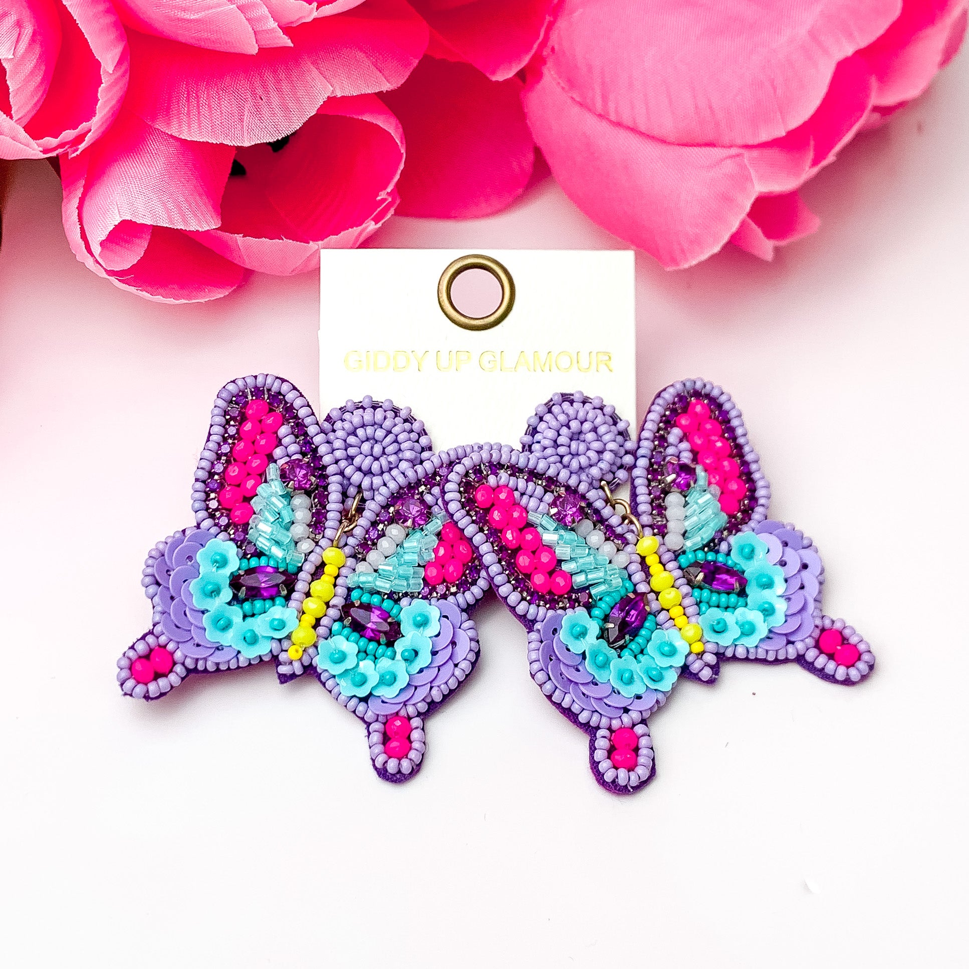 Purple beaded butterfly earrings. Pictured on a white background with pink flowers at the top.