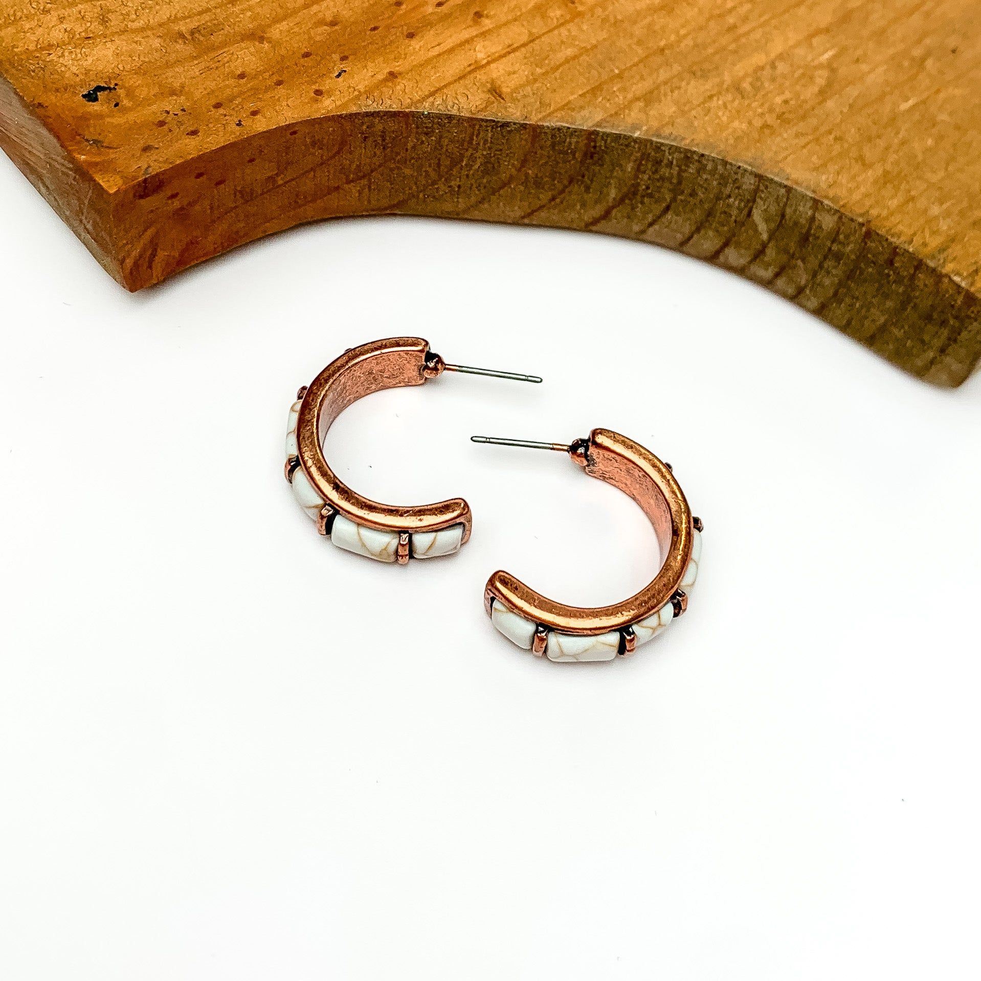 Ivory and copper tone medium hoop earrings. Pictured on a white background with wood at the top.