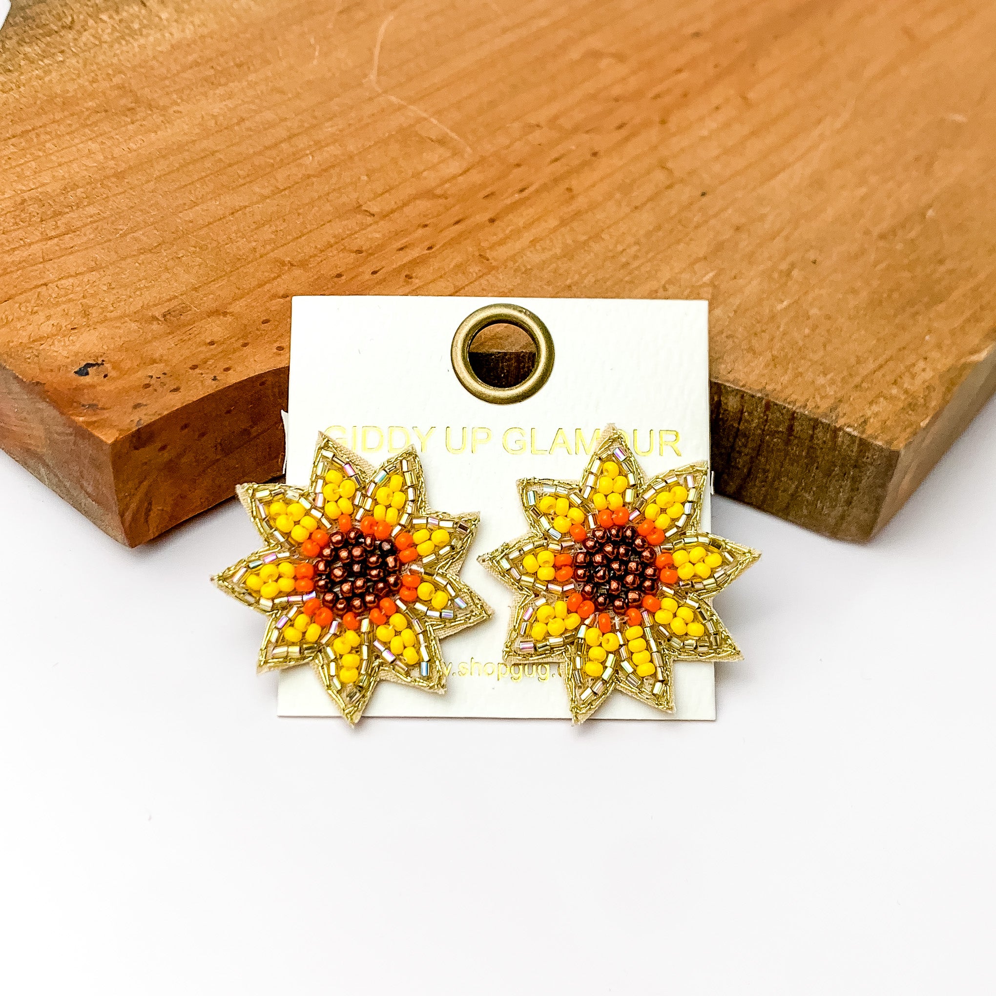 Beaded sunflower stud medium sized earrings.Pictured on a white background with a wood piece at the top.