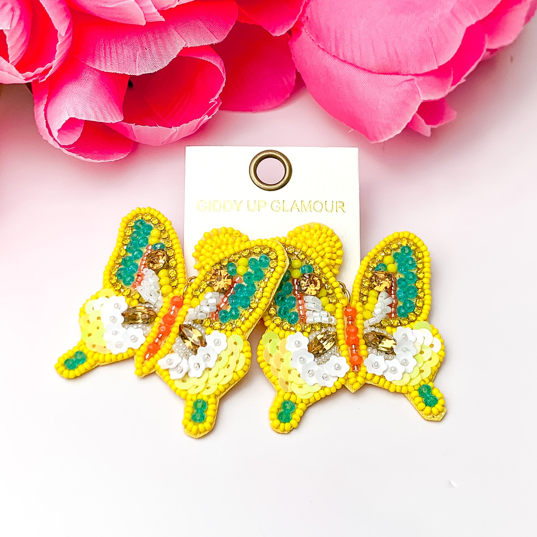Beaded yellow butterfly earrings. Pictured on a white background with pink flowers on top.