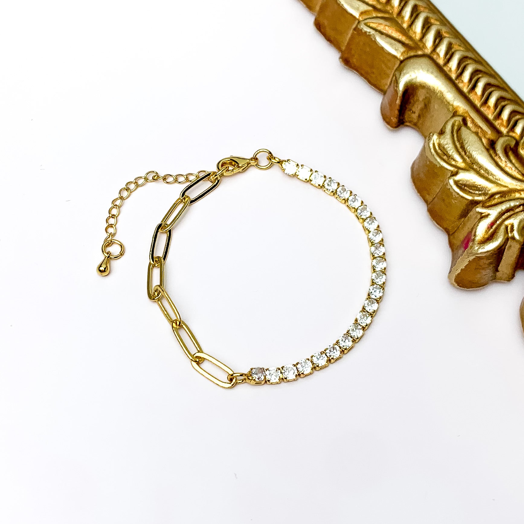 Pictured is half gold chain and half clear crystal, adjustable bracelet. This bracelet is pictured on a white background with a gold mirror shown in the top right corner.  