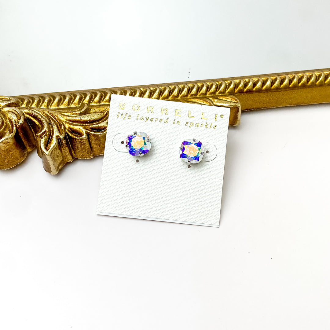 Pictured on a white cardstock is a pair of rounded square ab crystals with silver prongs. These earrings are pictured in front of a gold mirror on a white background. 