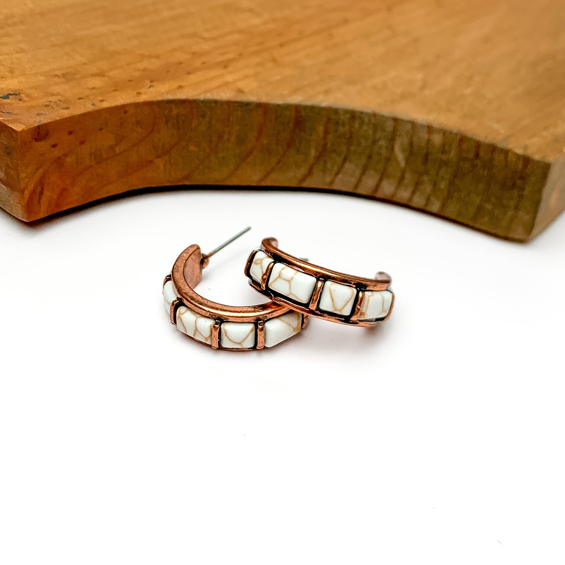 Ivory and copper tone medium hoop earrings. Pictured on a white background with wood at the top.