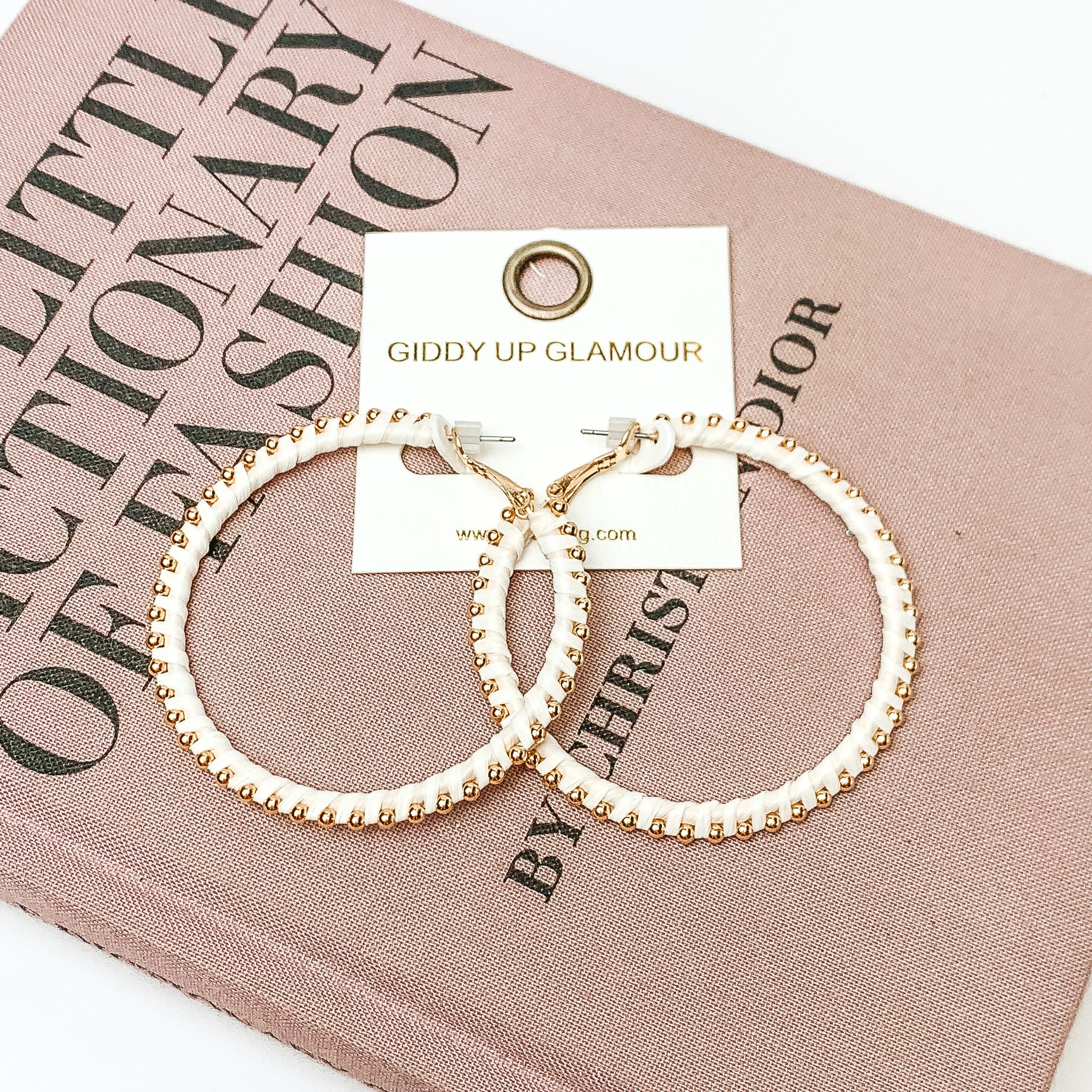 Pictured are circle ivory hoop earrings with gold beads around it. They are pictured with a pink fashion journal on a white background.