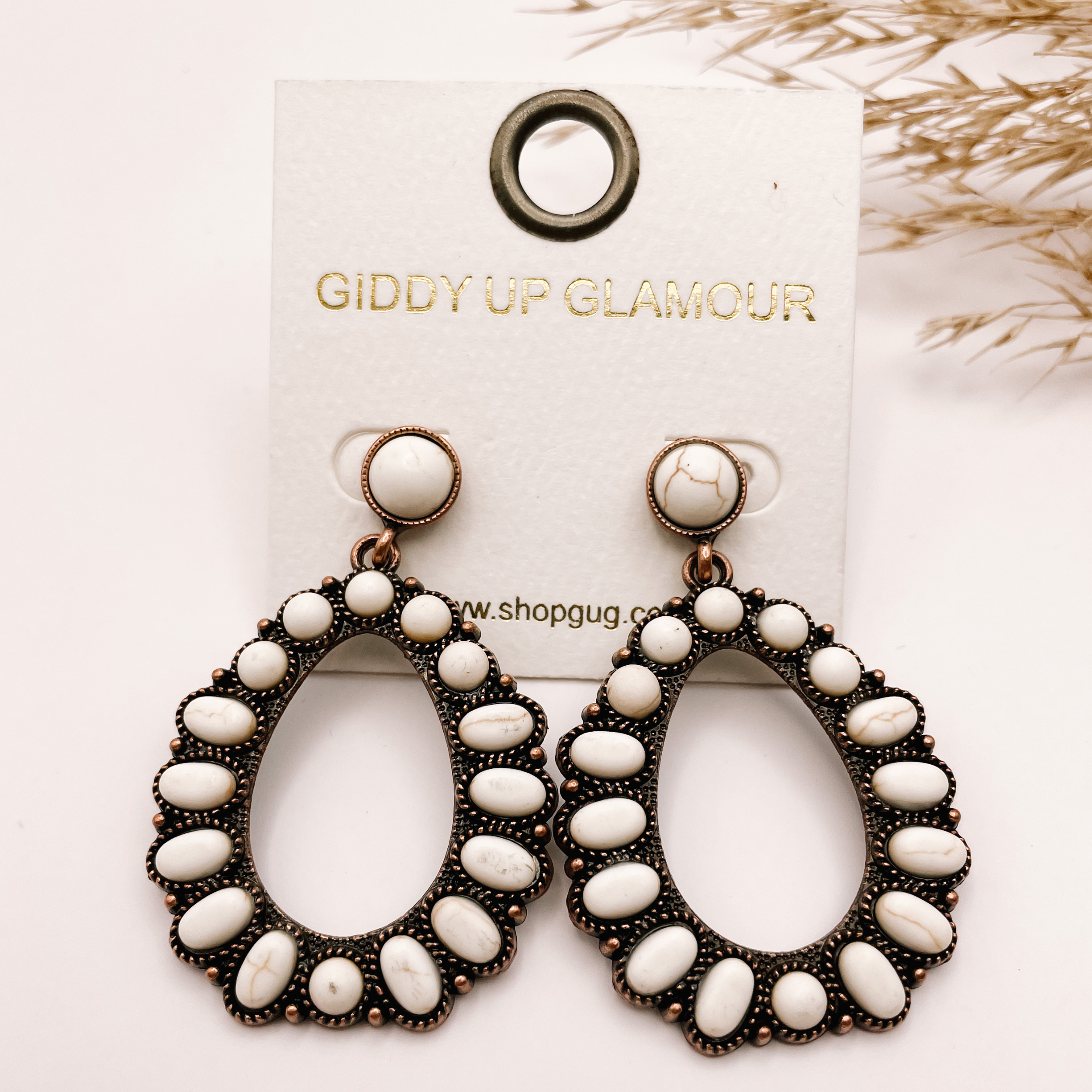 White stoned teardrop earrings, with pompous grass in the top right hand corner, on a white background.