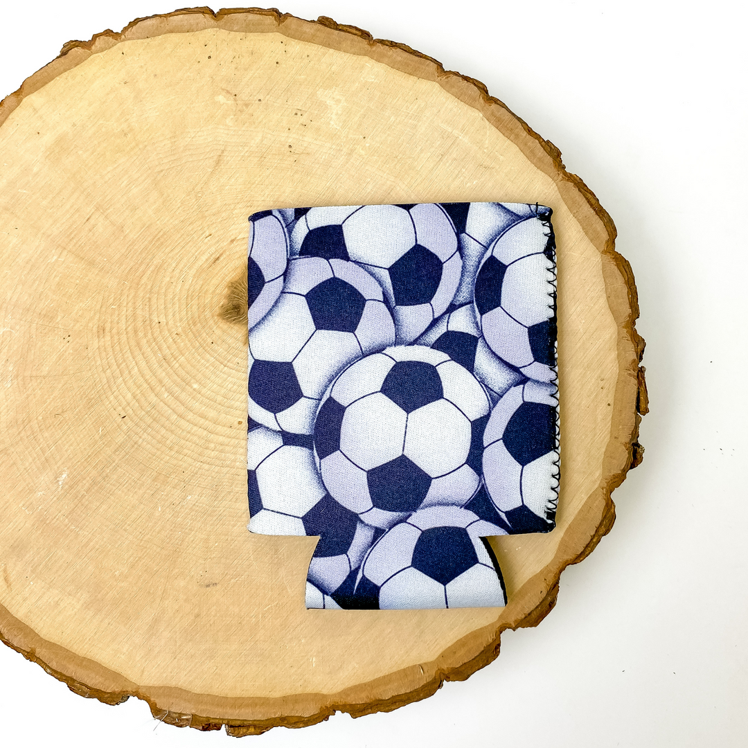 Soccer print koozie with black background. This koozie is pictured on a piece of wood on a white background.