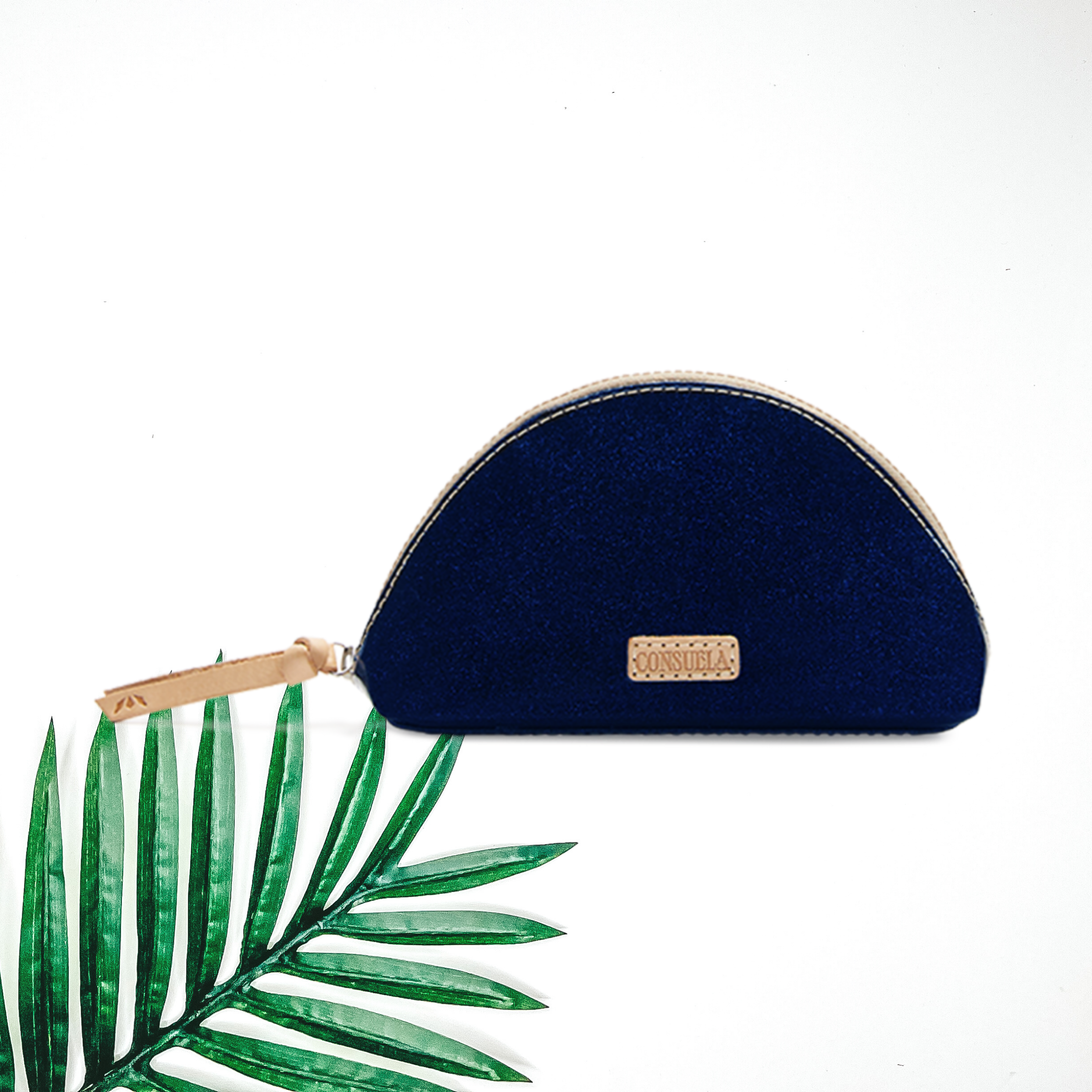Centered in the picture is a medium sized cosmetic case in a sparkly blue. A palm leaf is on the  bottom right, on a white background.  