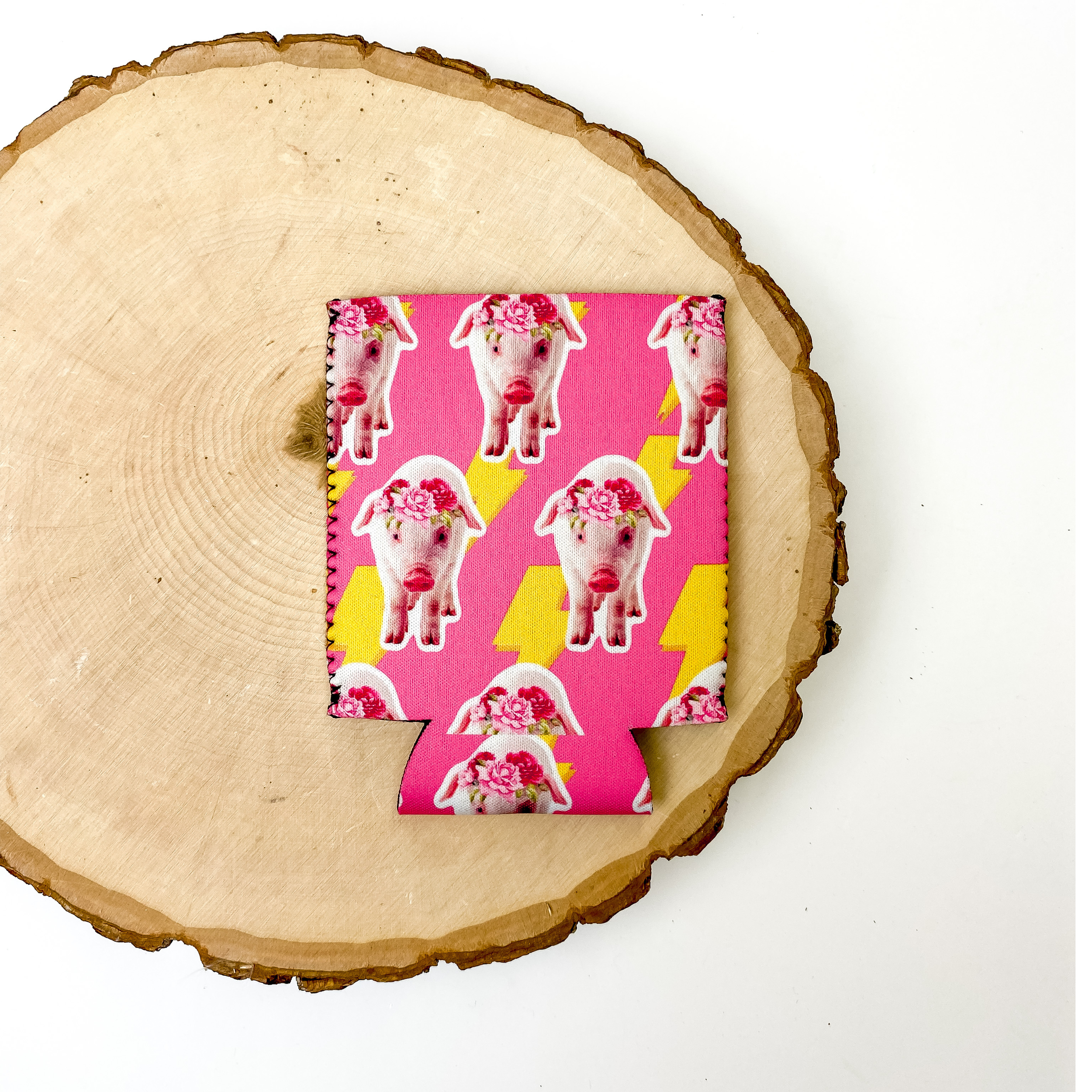 Hot pink koozie with pigs and yellow lighting bolts all over the koozie. This koozie is pictured on a piece of wood on a white background.