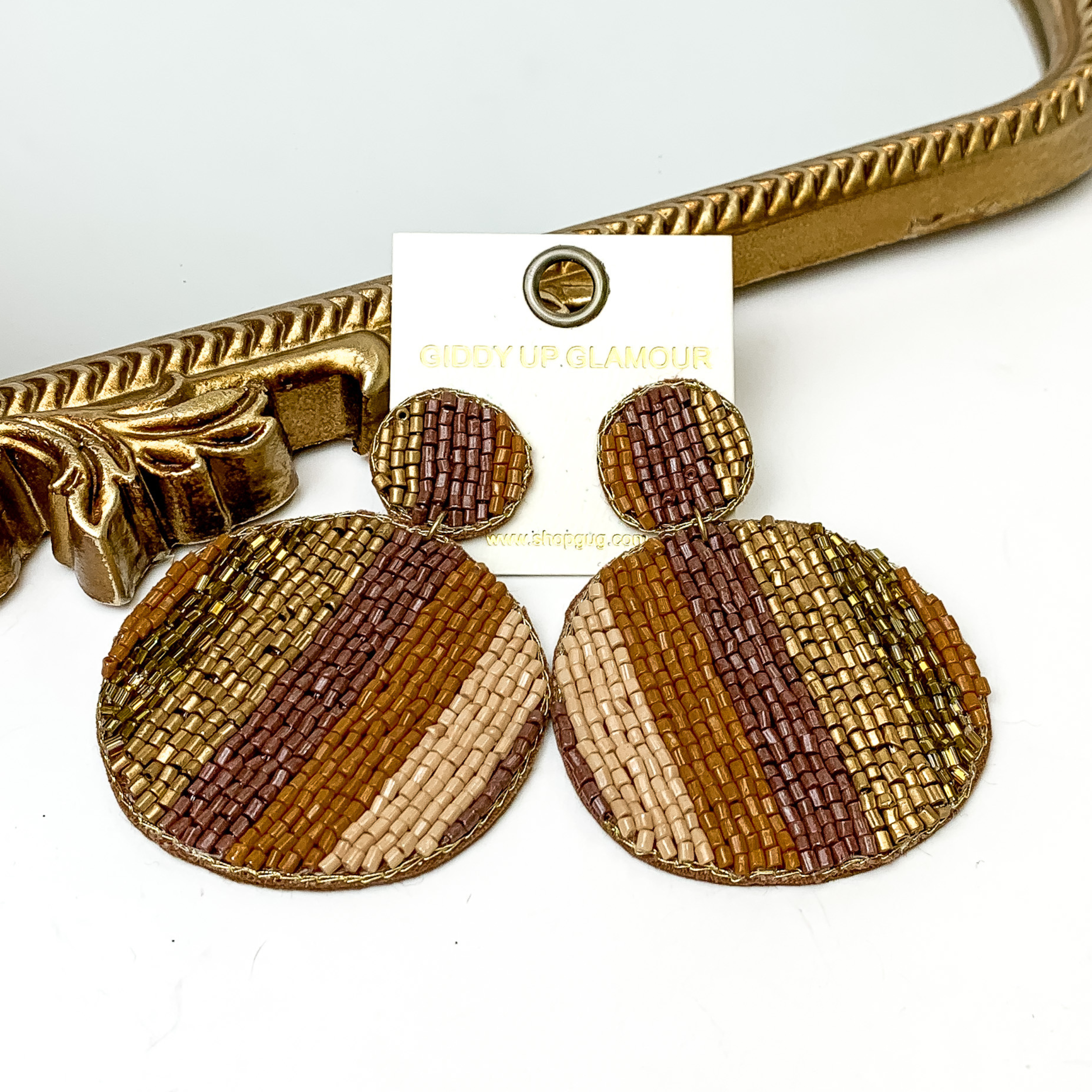 Pictured is a pair of beaded circle drop earrings in a stripe pattern. These earrings include multi colors of brown. These earrings are pictured in a white background with a gold mirror.