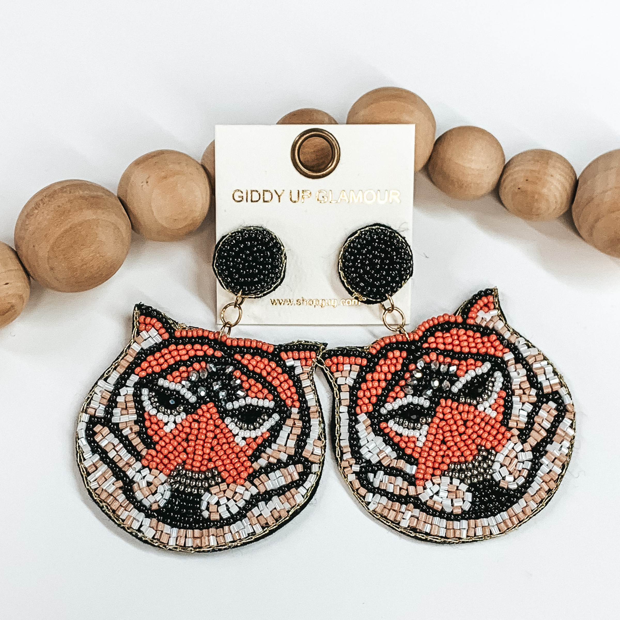 Tiger beaded drop earrings with black, orange, white,  peach, silver beads and silver crystals. Outlined in gold thread. Taken in a white background with  brown beads as decor.