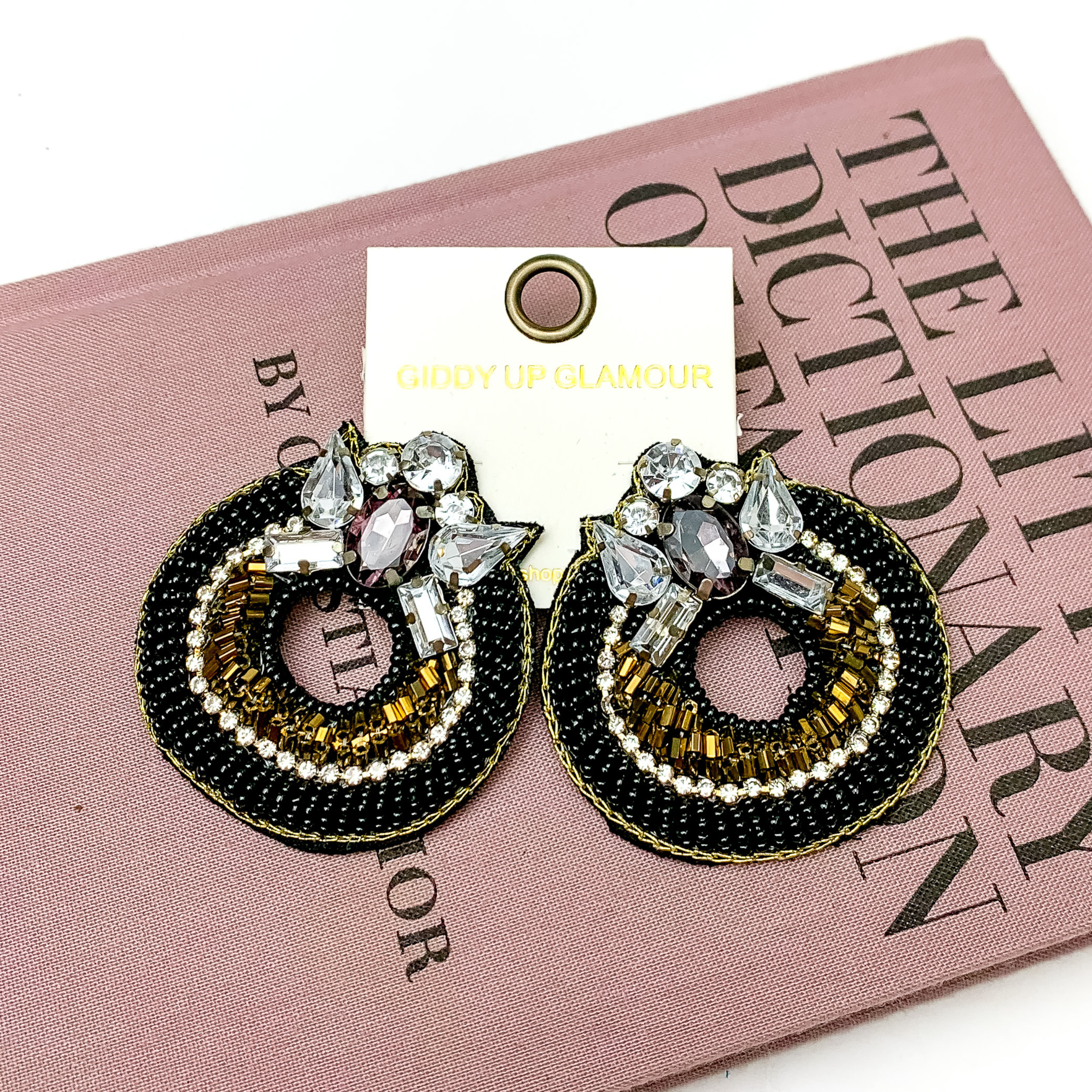 Pictured is a pair of beaded black earrings with a jeweled detail at the top. . These earrings are pictured in a white background with pink fashion dictionary.