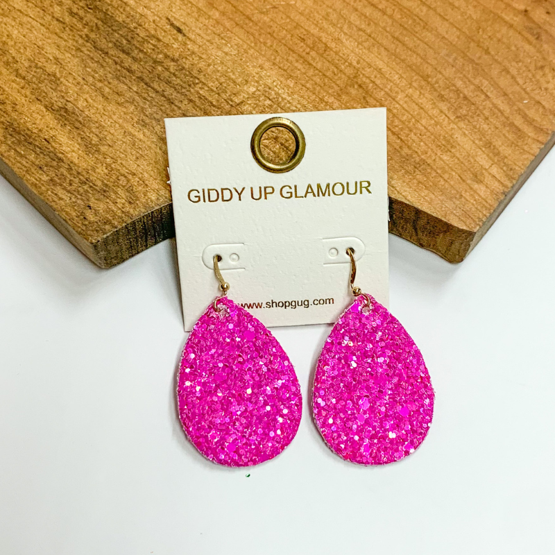 Pictured is pink glitter teardrop earrings. These earrings are pictured on a white background with a wooden board.