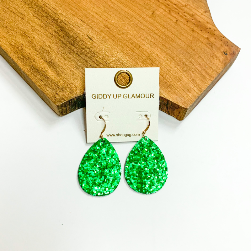 Pictured is green glitter teardrop earrings. These earrings are pictured on a white background with a wooden board.