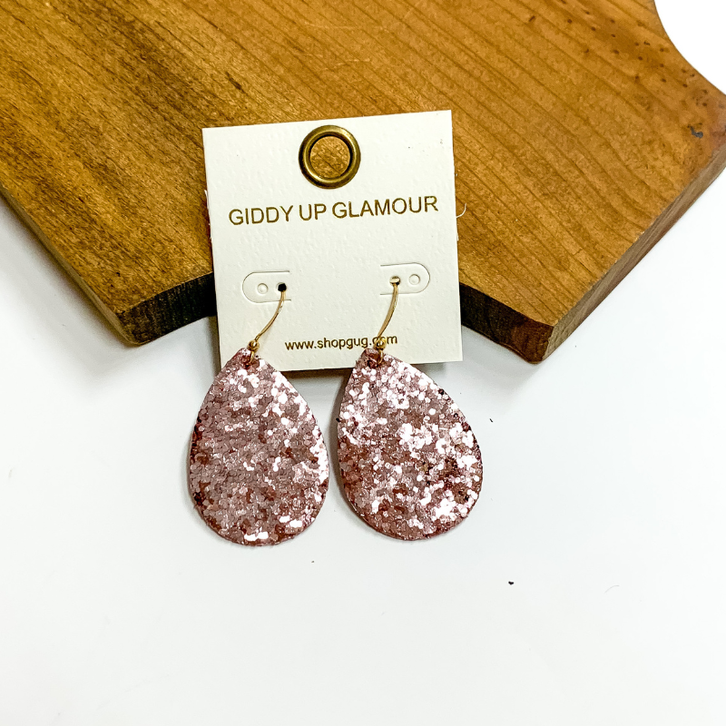 Pictured is rose gold glitter teardrop earrings. These earrings are pictured on a white background with a wooden board.