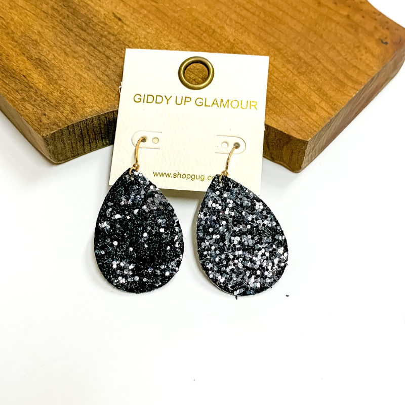 Pictured is black glitter teardrop earrings. These earrings are pictured on a white background with a wooden board.
