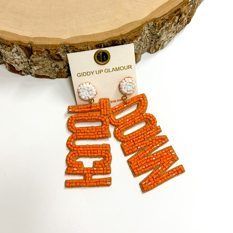 White circle post back earrings. These earrings include the words "Touch" and "Down" in orange beads. These earrings are pictured propped up on a circle piece of wood with white background.