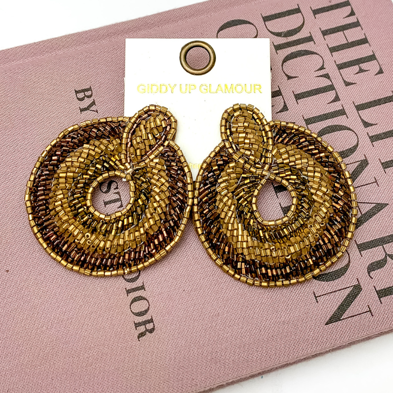 Pictured is hoop beaded brown and bronze earrings with. These earrings are pictured on a white background with a pink fashion dictionary.