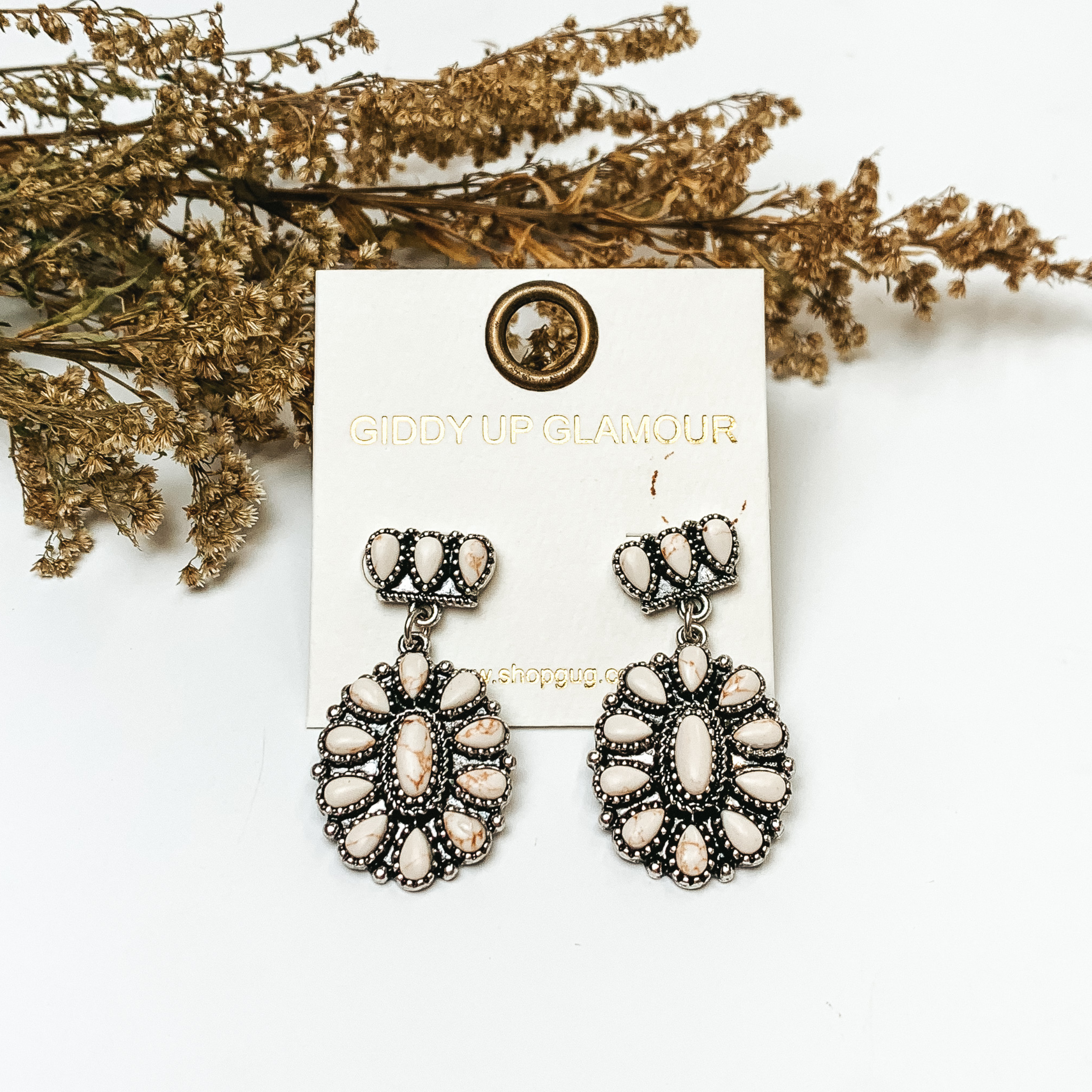 Silver tone cluster post earrings with oval cluster drop with ivory stones. These earrings are pictured on a white background with greenery behind the earrings.