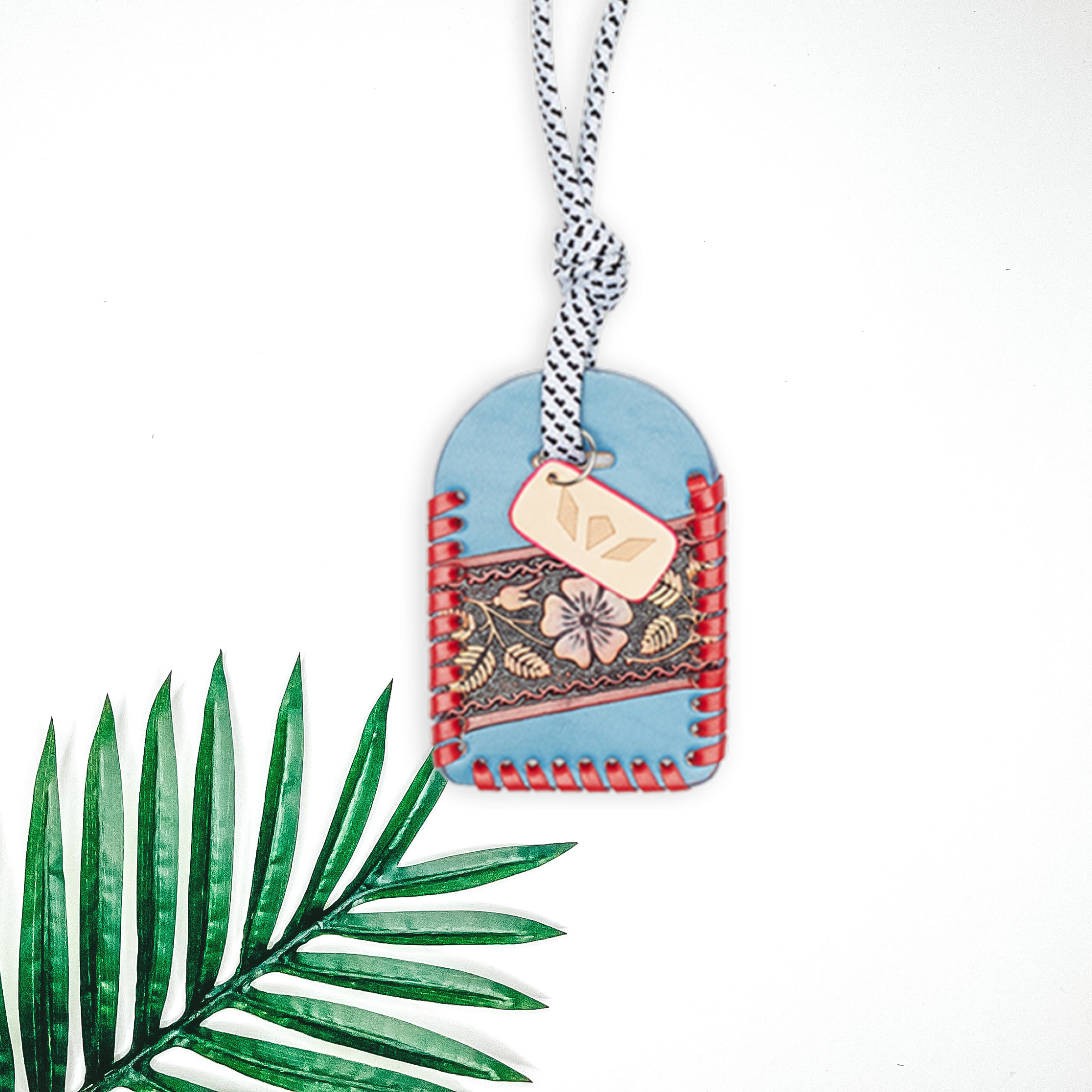 Pictured is a luggage tag in blue and red. to the leeft of the tag is a palm leaf on a white background. 
