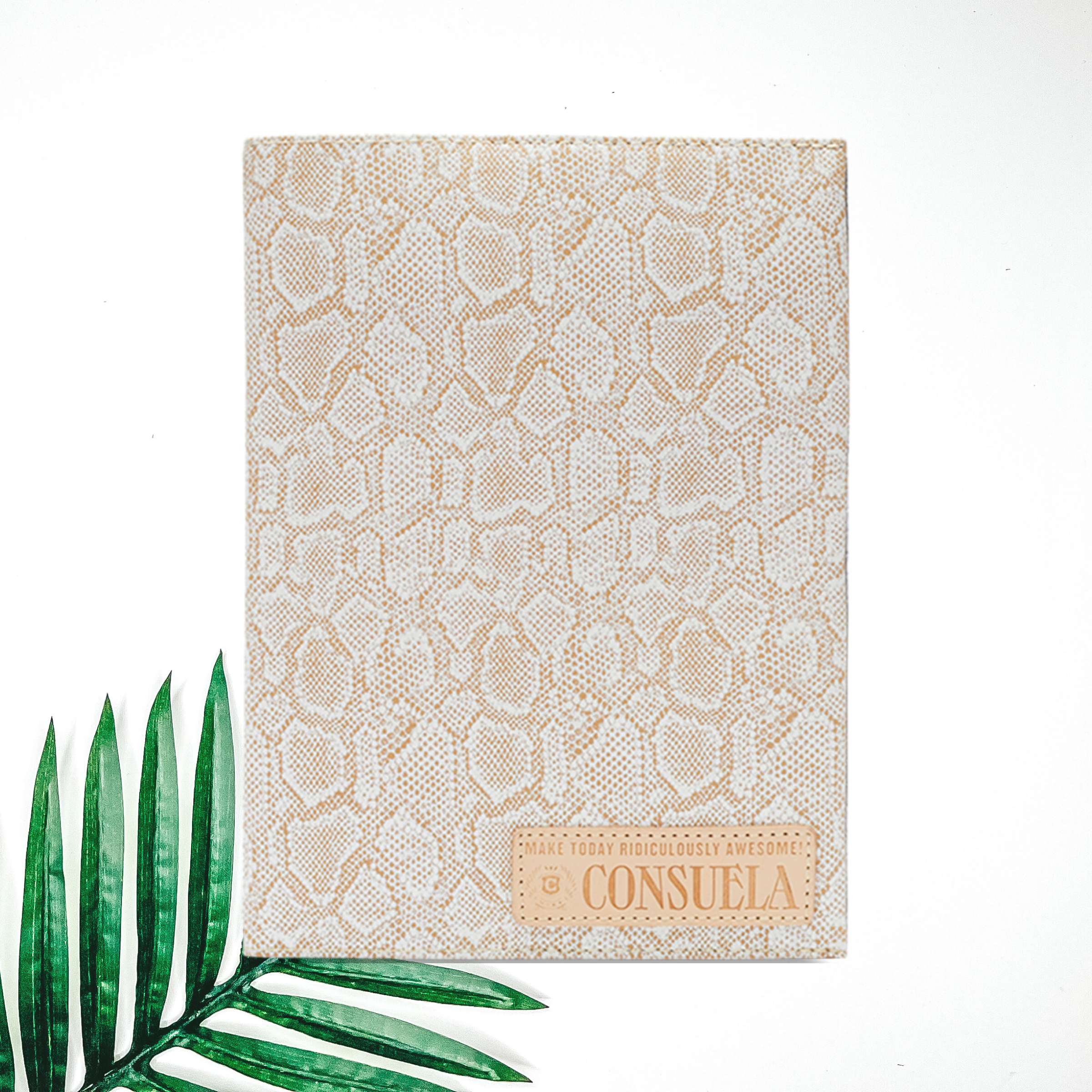 Centered in the picture is a notebook white snakeskin. To the right of the notebook is a palm leaf, all on a white background.