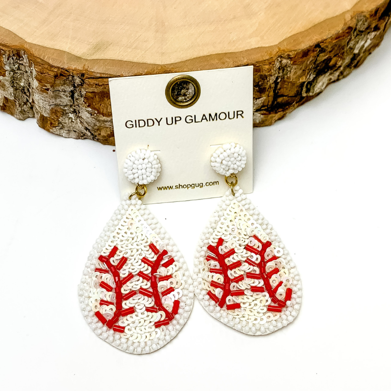 Pictured are teardrop sequin baseball earrings with beaded detailing. These earrings are propped up on a circle piece of wood on a black background