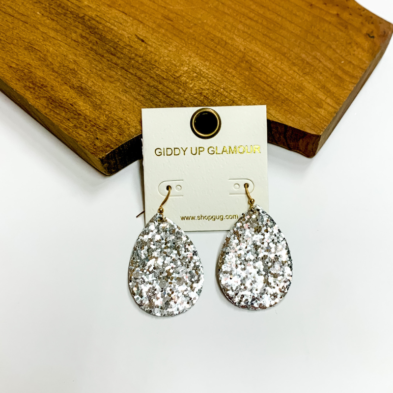 Pictured is silver glitter teardrop earrings. These earrings are pictured on a white background with a wooden board.
