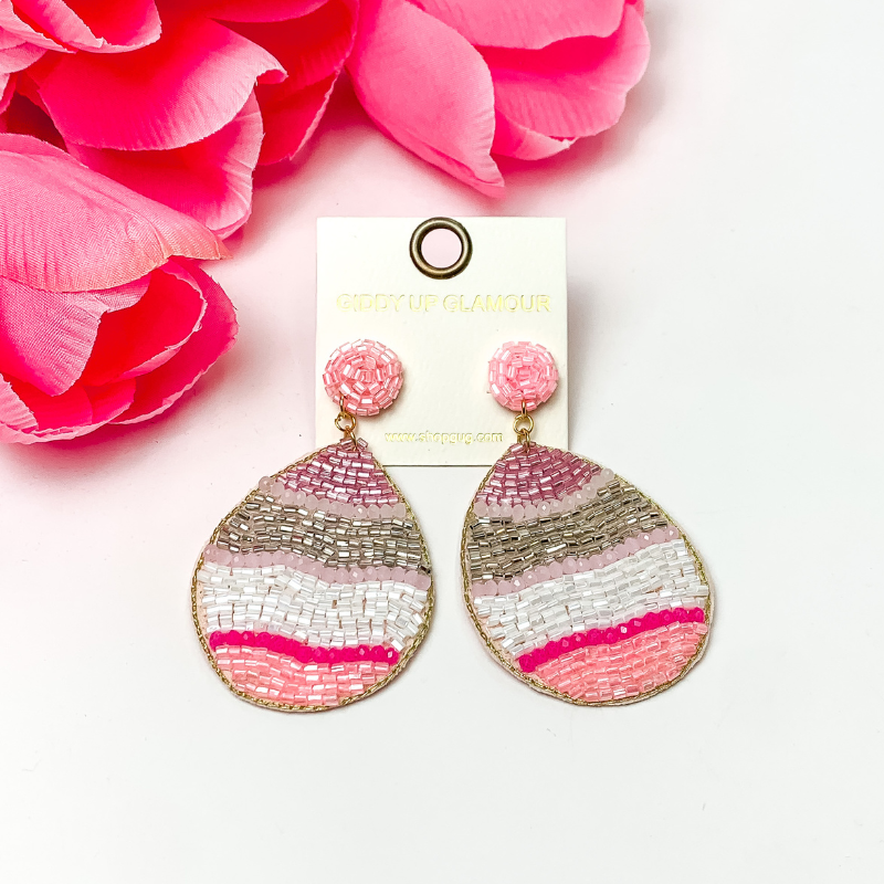 Beaded multi pink and white Easter egg. These earrings are pictured on a white background with red-coral flowers at the top left corner.