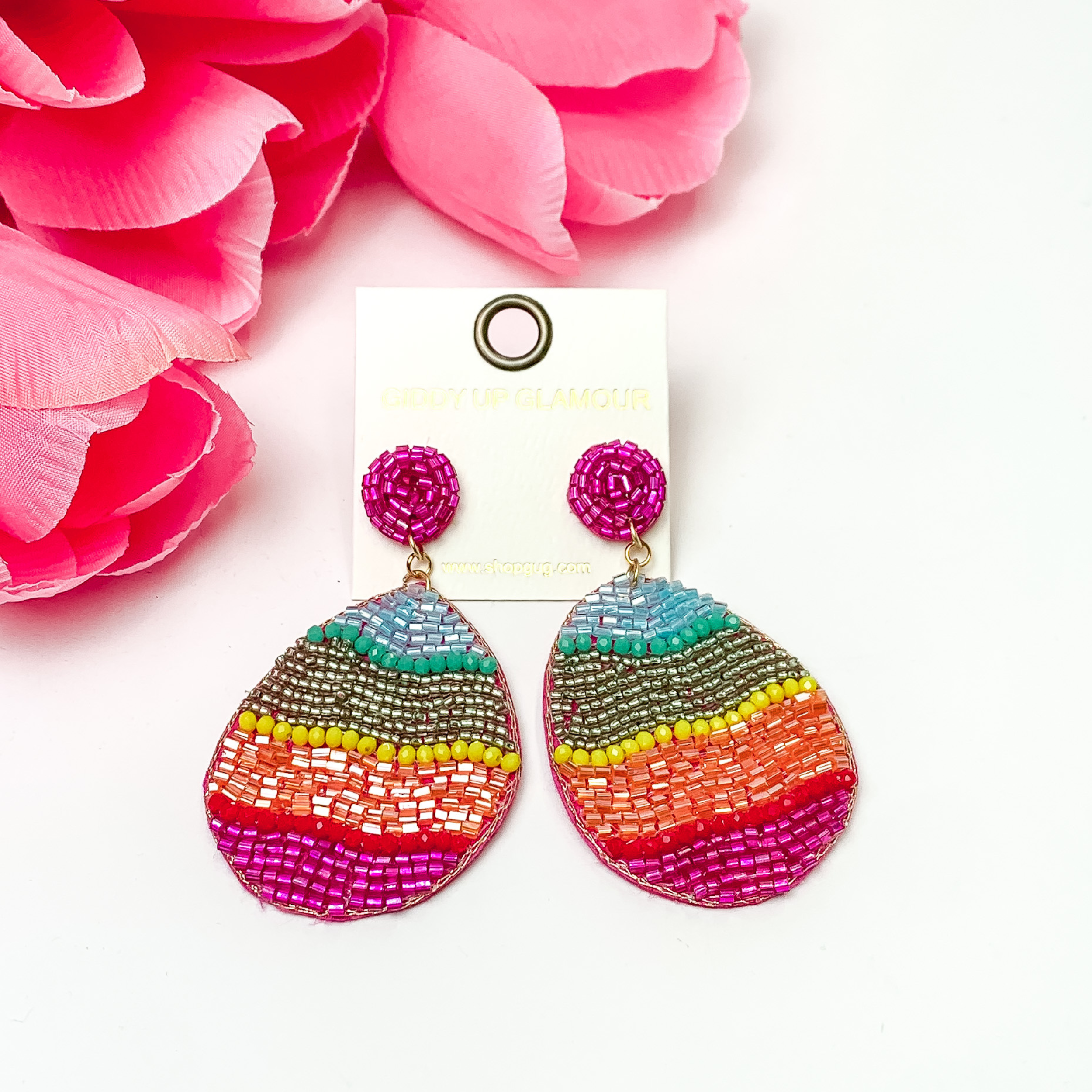 Beaded multi colored Easter egg. These earrings are pictured on a white background with red-coral flowers at the top left corner.