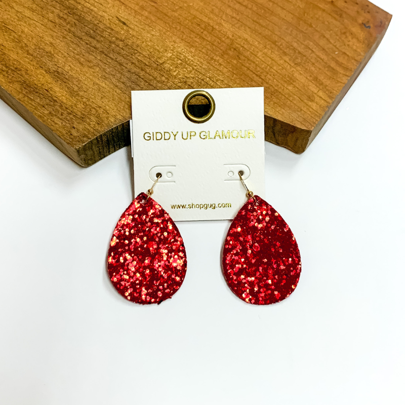 Pictured is red glitter teardrop earrings. These earrings are pictured on a white background with a wooden board.