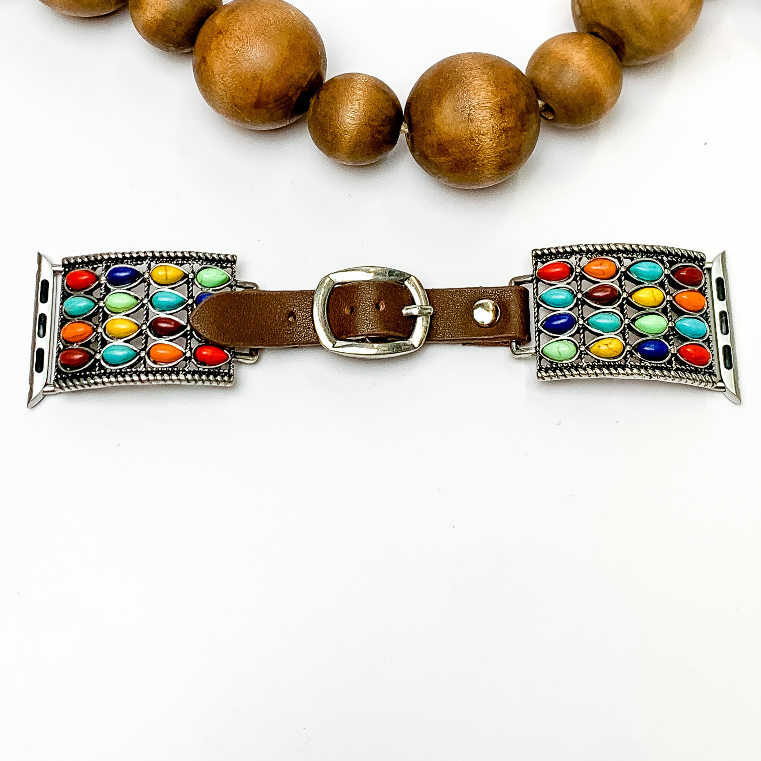  Dark Brown watch band with silver multicolor stones detail with Apple watch band acessories. The watch band has a western pendant with multiple colored stones. This watch band is pictured on a white background with wooden brown beads above the watch.