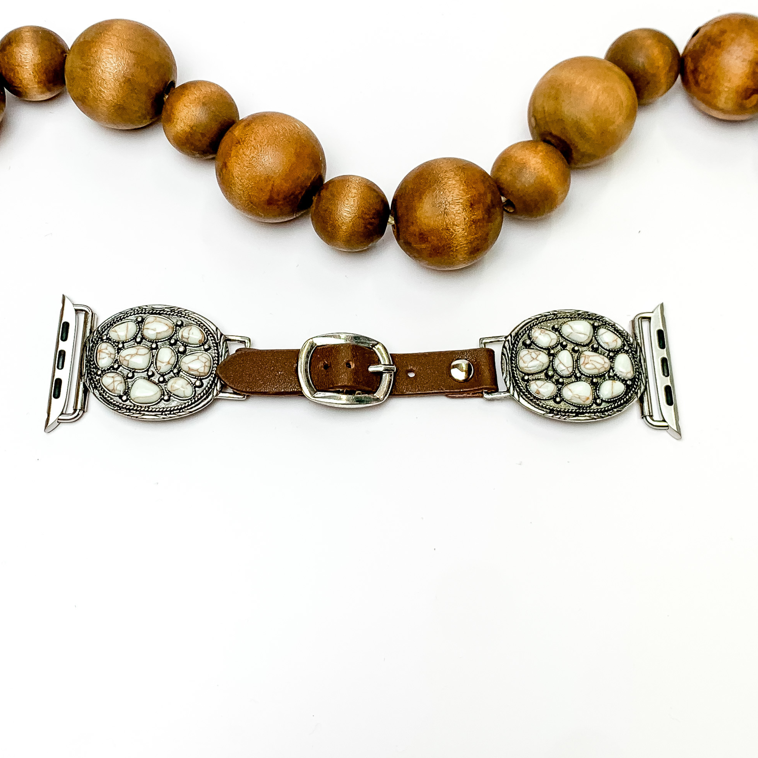Brown smart watch band with s cluster of white stones in each side. The smart watch has to oval shape silver pendants and in each one there is a cluster of white stones in a circle. The watch is pictured on a white background with wooden beads above the watch.