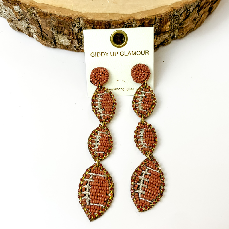 Pictured are dangly circle beaded post back football earrings in brown. They are propped up against a circular piece of wood on a white background.