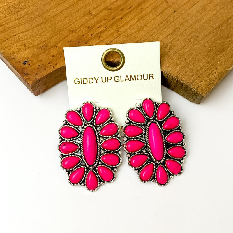 Pictured is western pink oval cluster earrings. They are propped up against a wood board on a white background. 