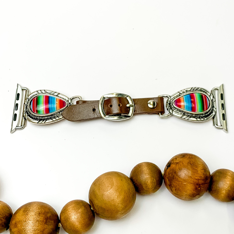 Pictured is a brown smart watch band with teardrop serape stones. They are pictured with brown wooden beads below the band on a white background.