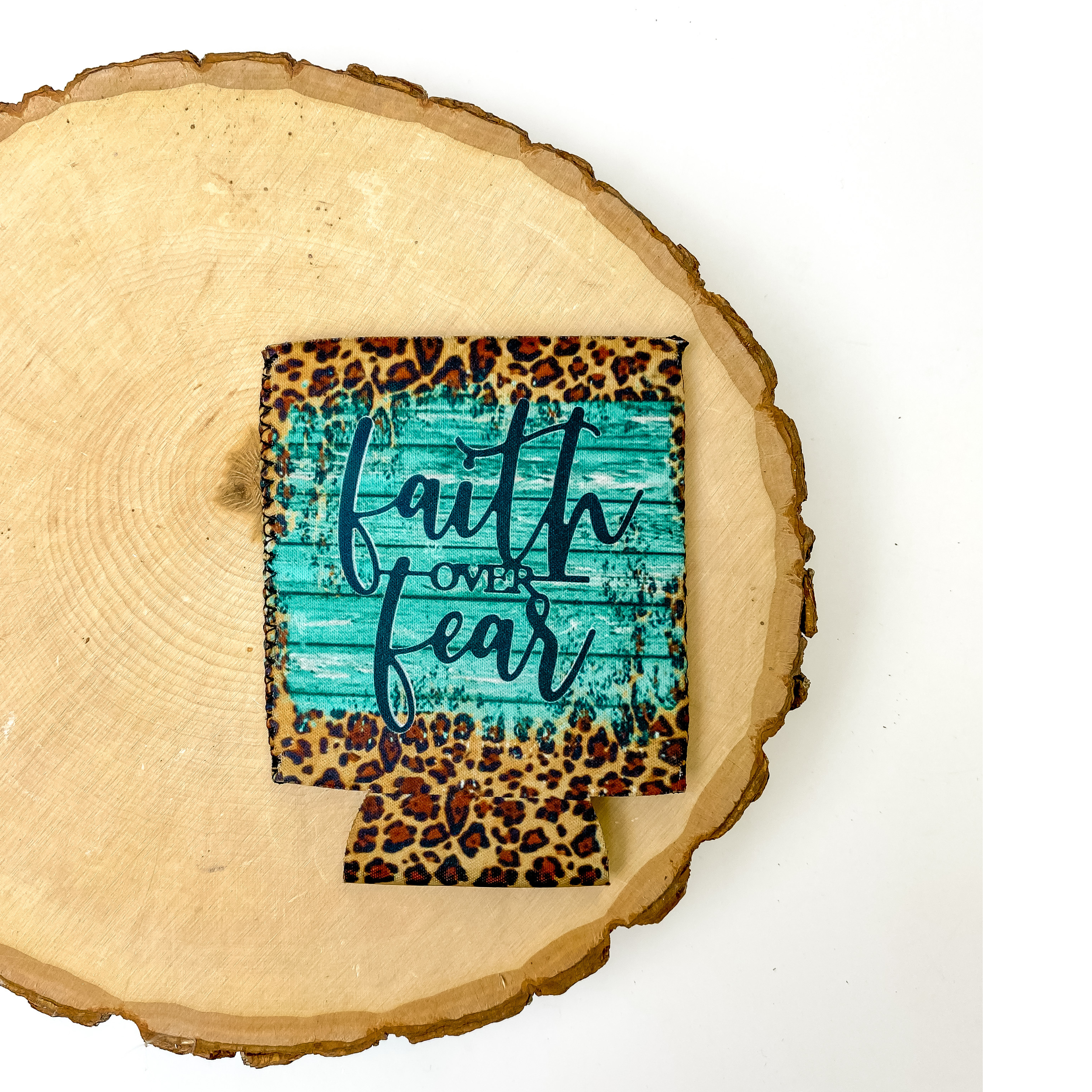 Koozie with the saying "Faith over fear" with turquoise and leopard print background. This koozie is pictured on a piece of wood on a white background.