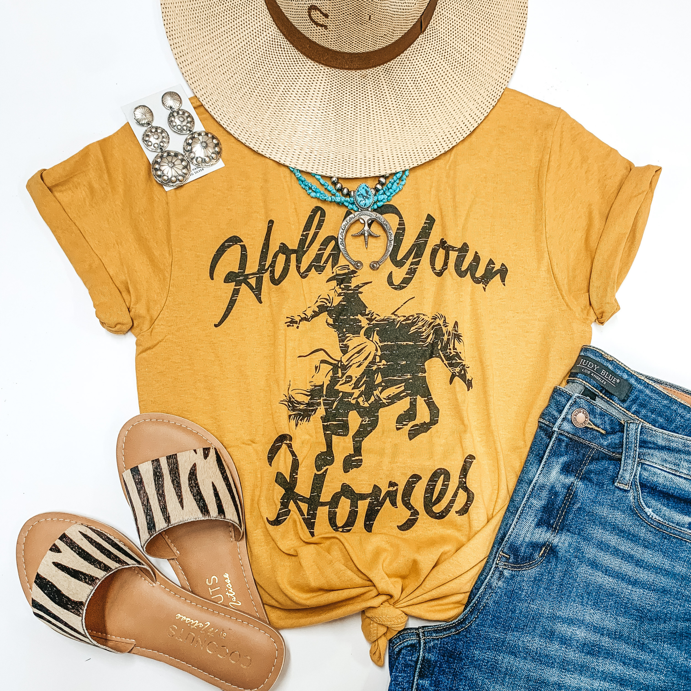 A mustard yellow graphic tee with a cowboy that says "Hold your horses." Pictured with sandals, denim shorts, and genuine Navajo jewelry.