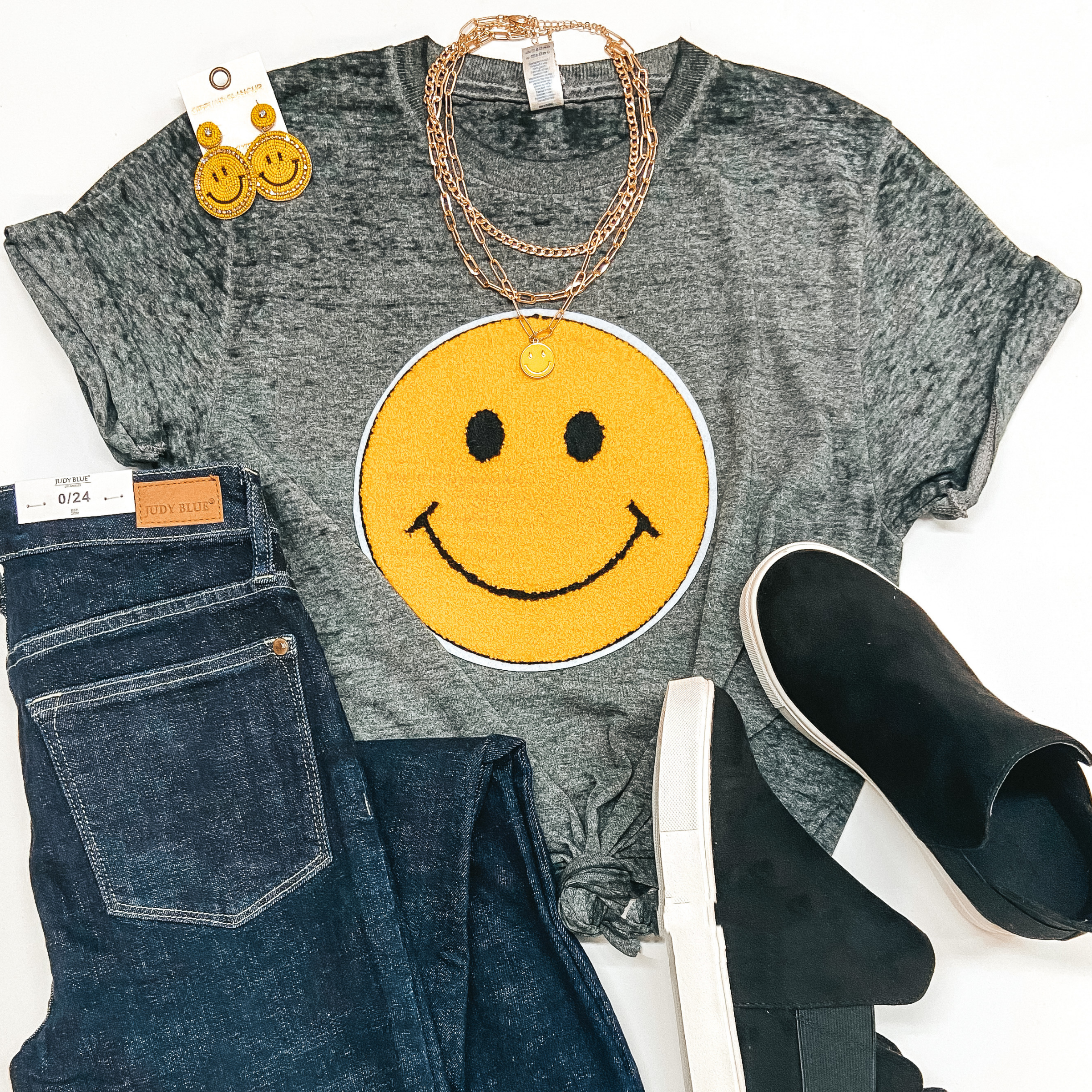 Fuzzy Patch Smiley Face Graphic on Grey Acid wash tee. Pictured with skinny jeans, black heeled sneakers, and smiley face jewelry