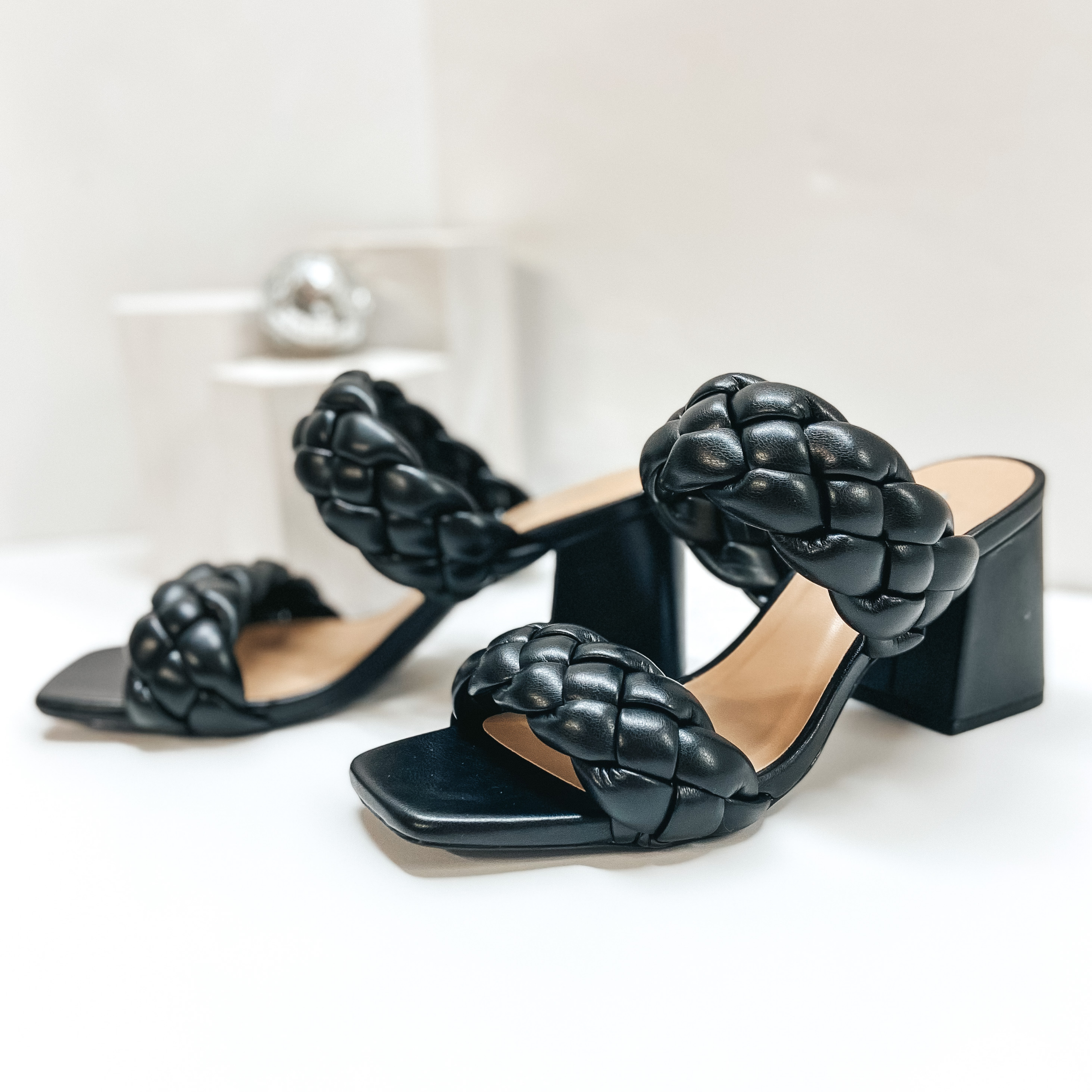Black braided block heels with two staps. Pictured against a white background.
