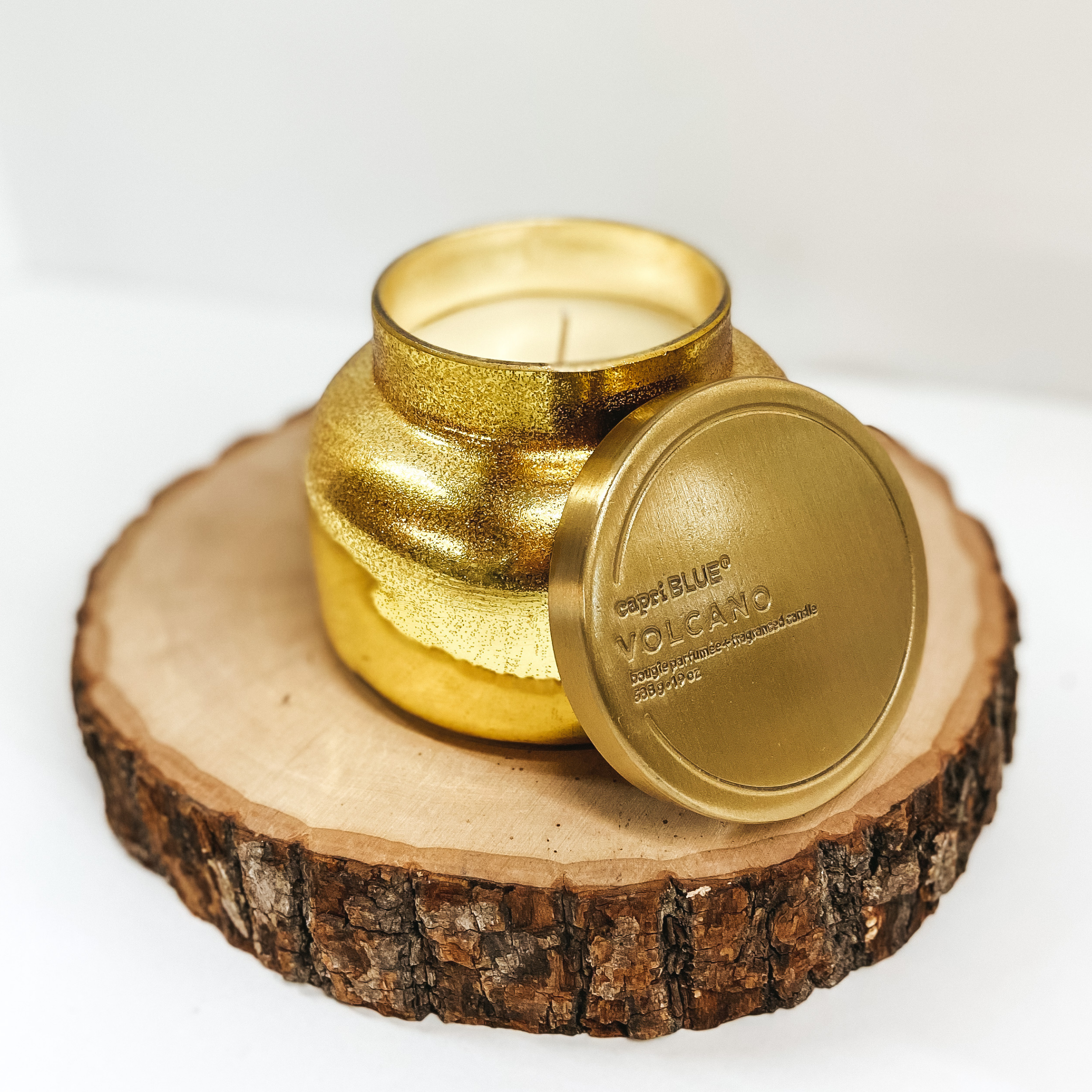 Gold glitter jar candle pictured on wooden stump against a white background.