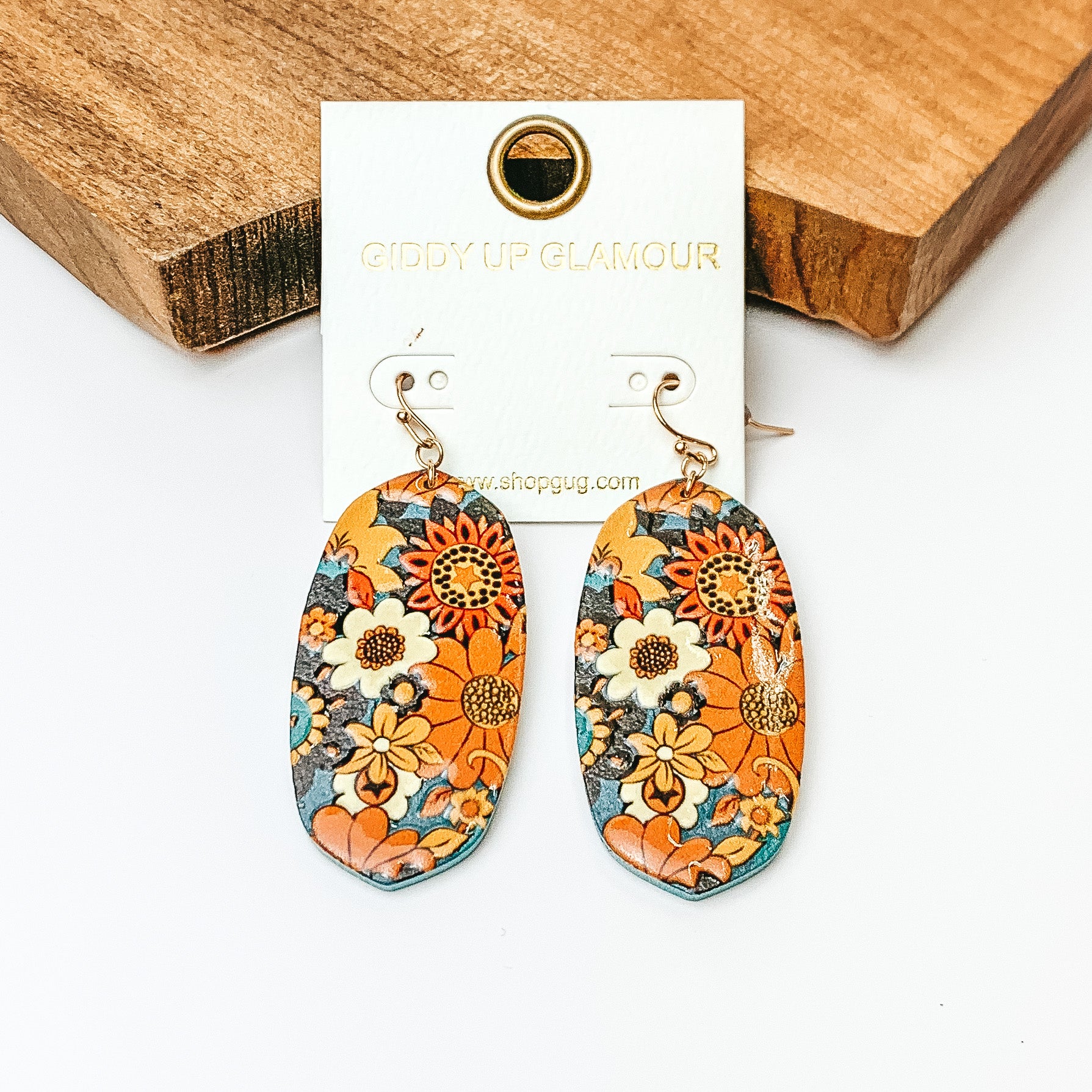 Pictured are oval drop earrings on gold fish hooks. These earrings have floral print in a mix of navy and rust. These earrings are pictured on a white background in front of a wood block. 