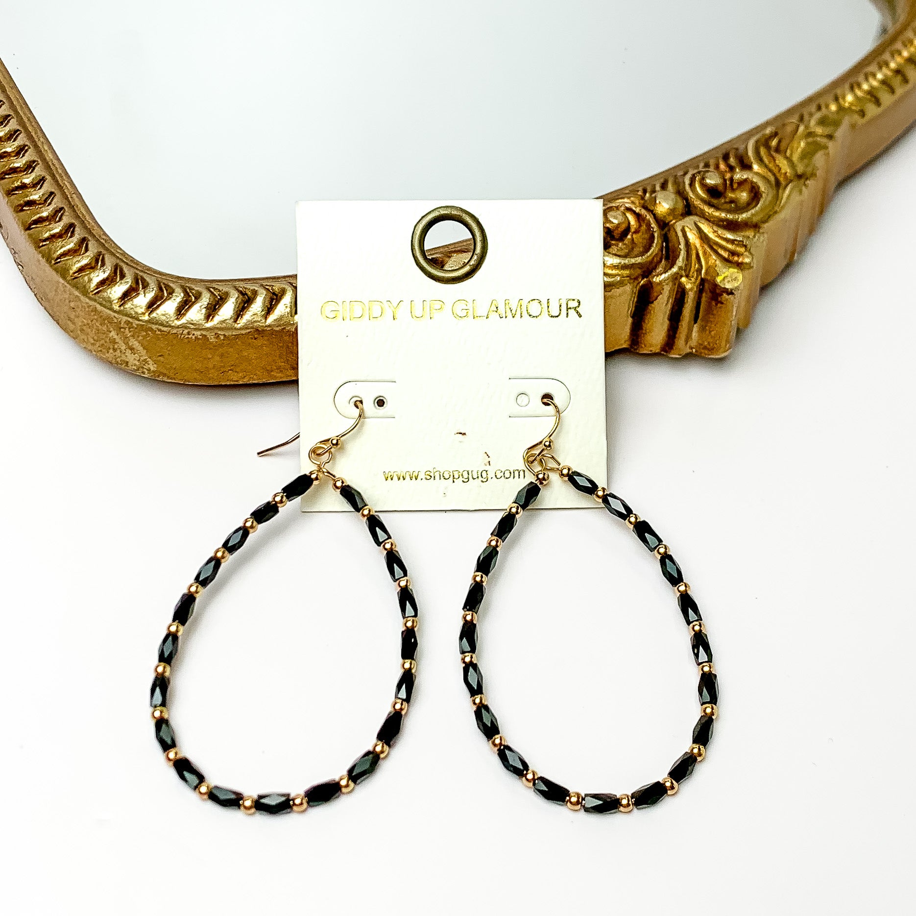 Black beaded open drop earrings with gold tone features. Pictured on a white background with a gold frame through it.