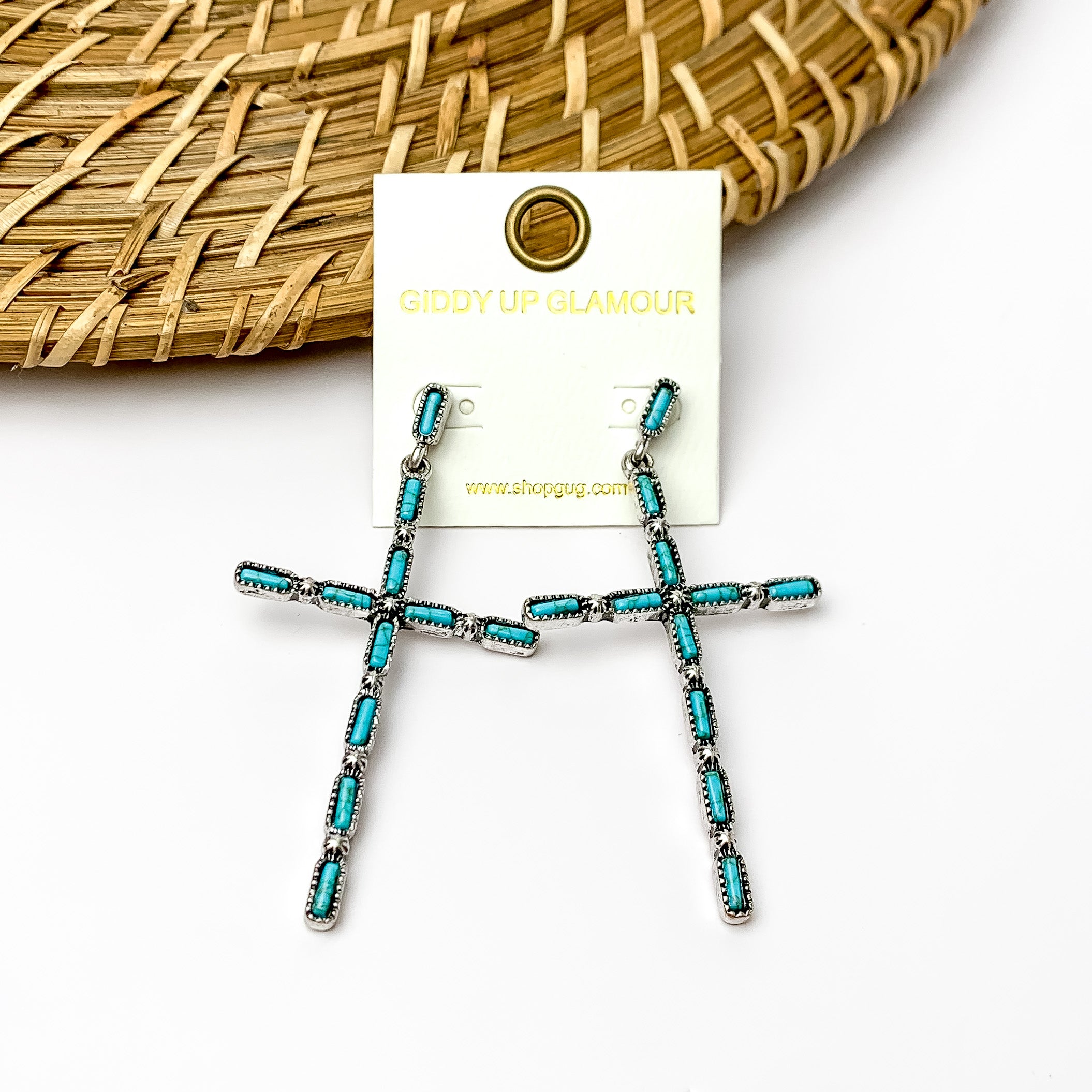 Turquoise and silver tone western cross earrings. Pictured on a white background with a wood like piece at the top.