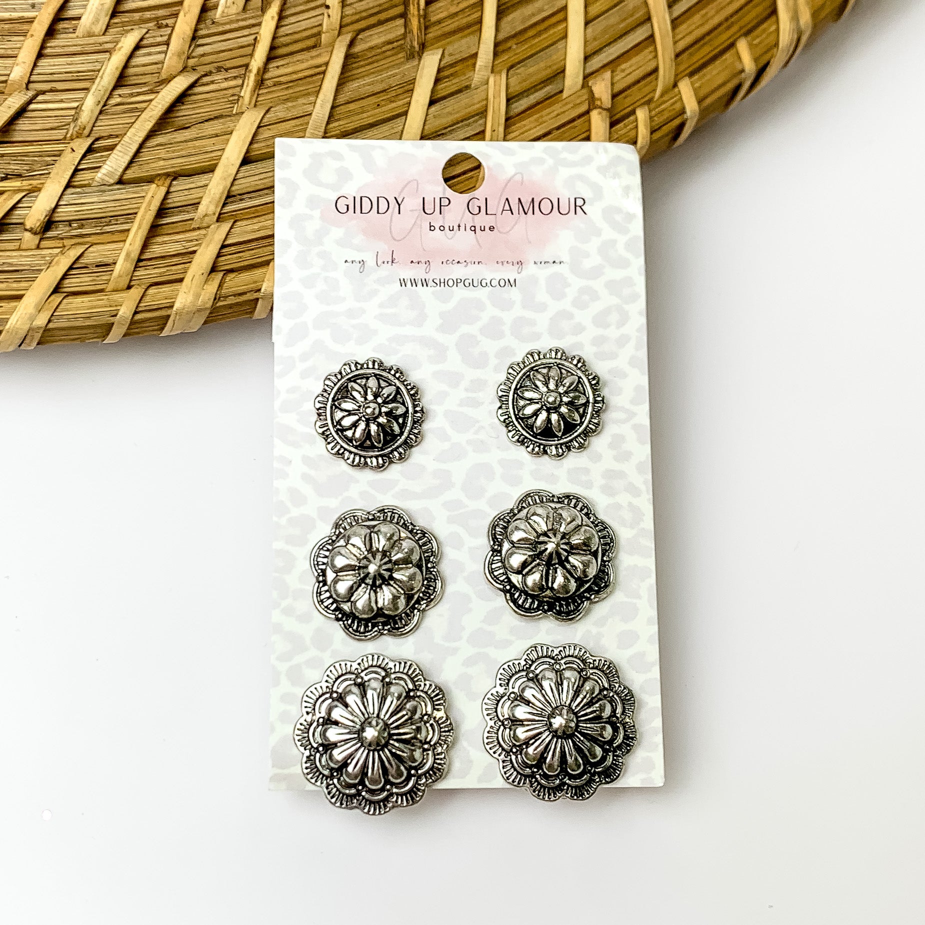 Three pairs of silver tone designed circular stud earrings. Pictured with a white background and a wood like decoration in the top left corner.