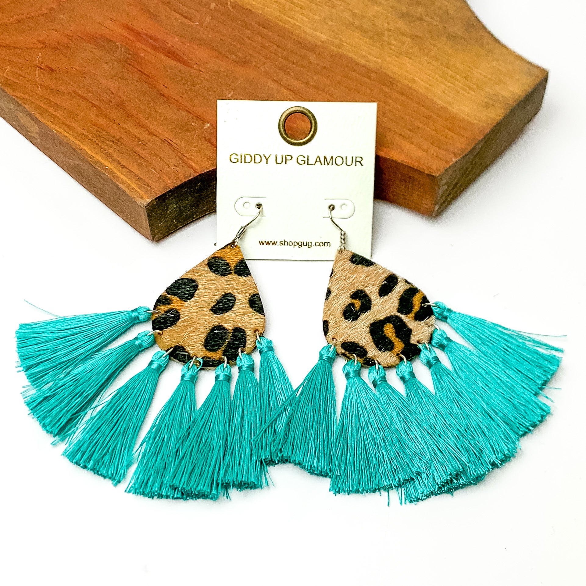 Leopard print drop earrings with turquoise tassels. Pictured on a white background with a wood piece at the top.