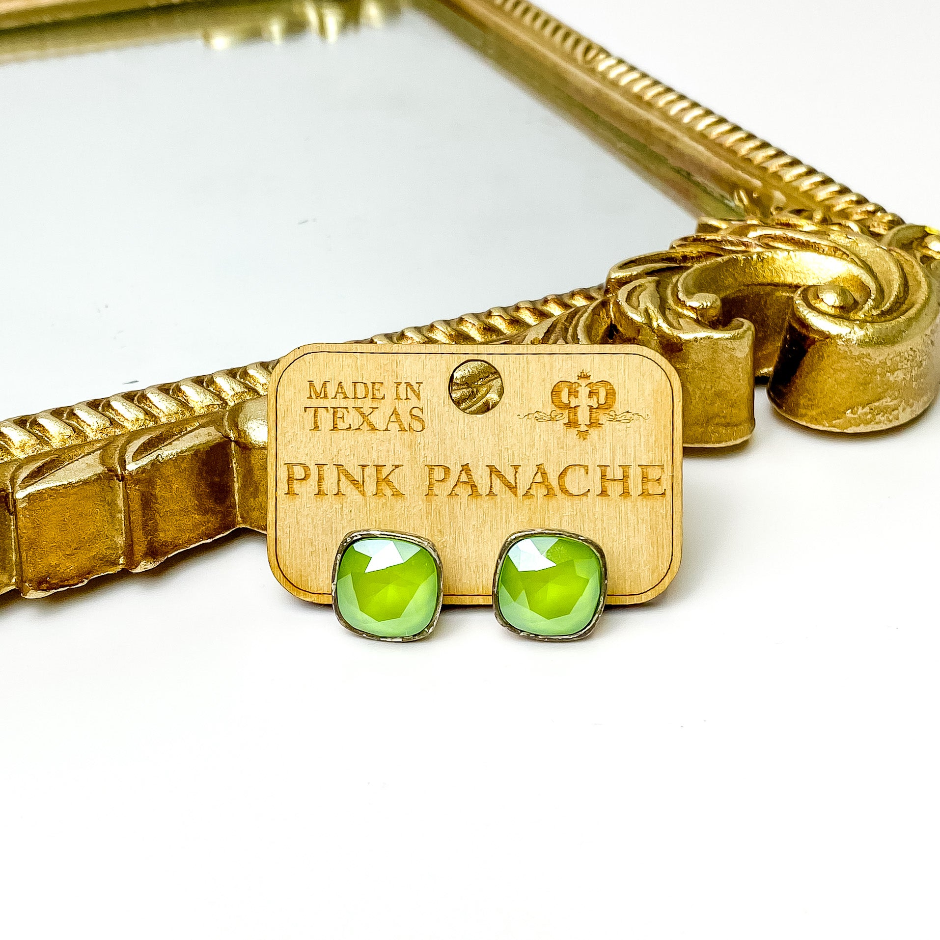 Lime green cushion cut crystal stud earrings with a silver setting. These earrings are pictured on a Pink Panache wood holder in front of a gold mirror and on a white background.